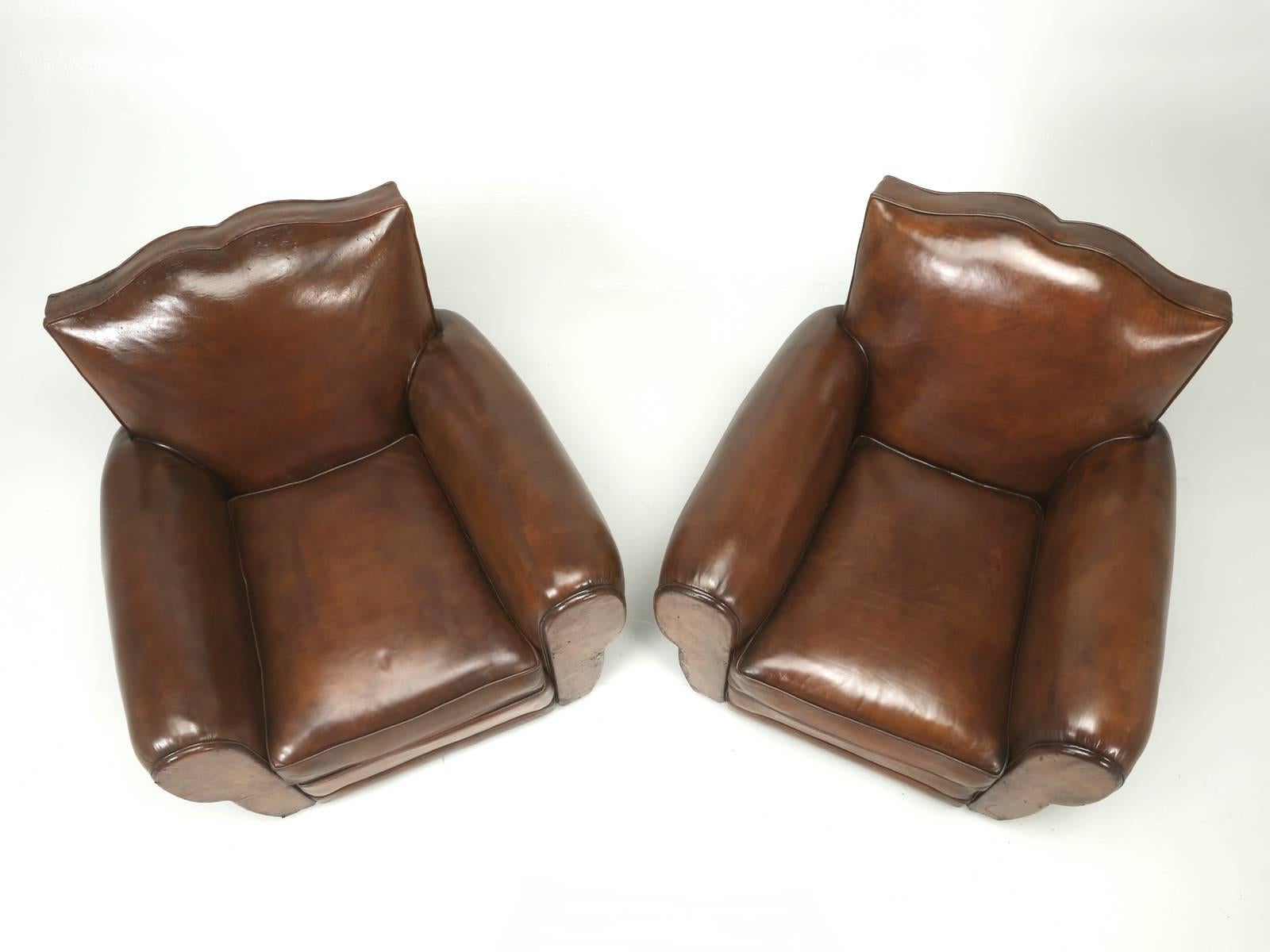 Matched pair of French Art Deco “Moustache” original leather club chairs. Our in-house upholstery department, carefully disassembled the chairs down to their bare wood frame and began the laborious task of rebuilding everything from the ground up,