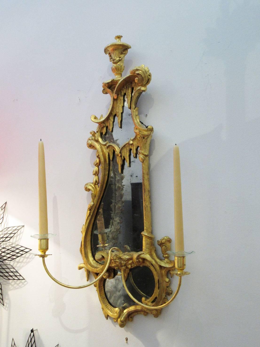 Pair of antique 18th century George III wall sconces with asymmetrical mirrors and candle holders. Frames are ornately carved giltwood with sweeping 'C' curves, rocaille, and relief decoration. Each sconce has two adjustable candle holders that can