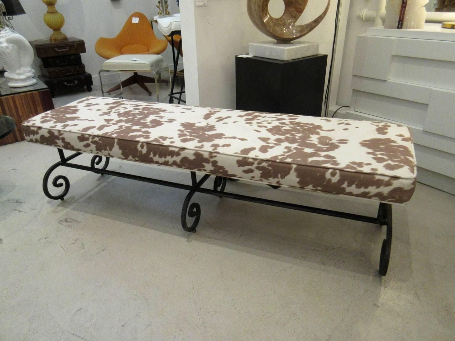Black long wrought iron bench that rests on six small brass ball feet. Upholstered in faux cowhide.