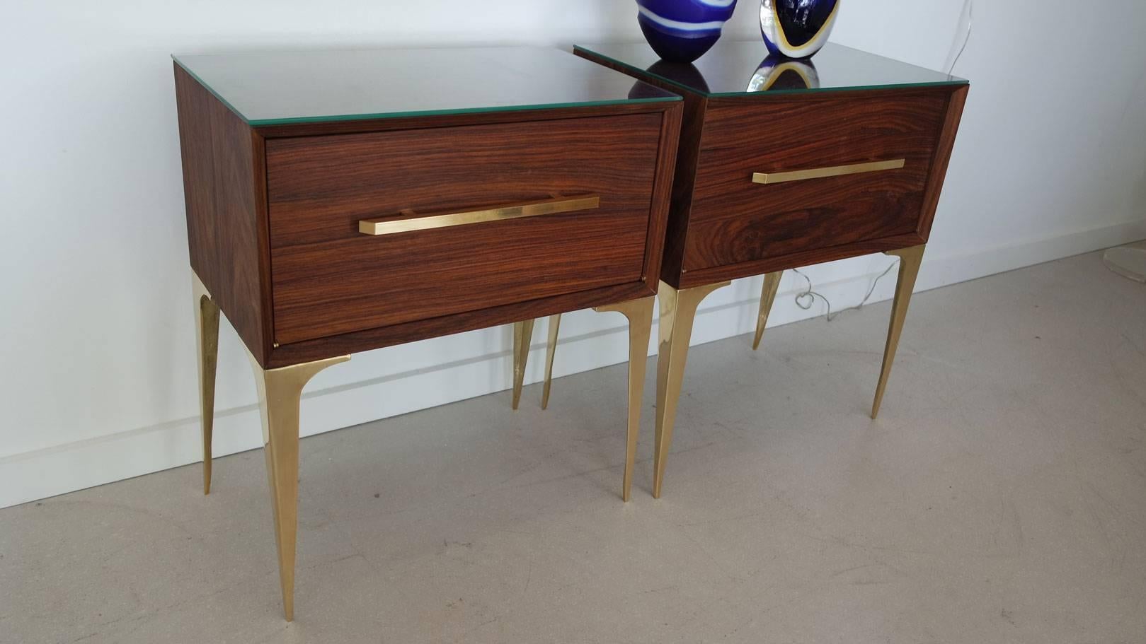 Pair of Mid-Century Modern palisander wood bedside tables with brass hardware and legs, and topped with glass.  Flip down fronts with open insides, both have been completely refinished and restored.