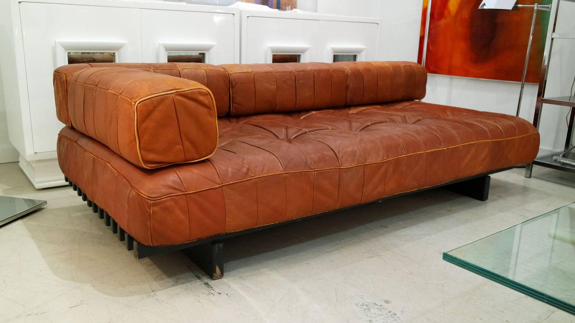 Vintage cognac colored leather daybed by De Sede of Switzerland. The daybed has modular back cushions which rest on a black slat wood platform. All the leather is in good condition without rips or tears but attractive signs of age. It has been
