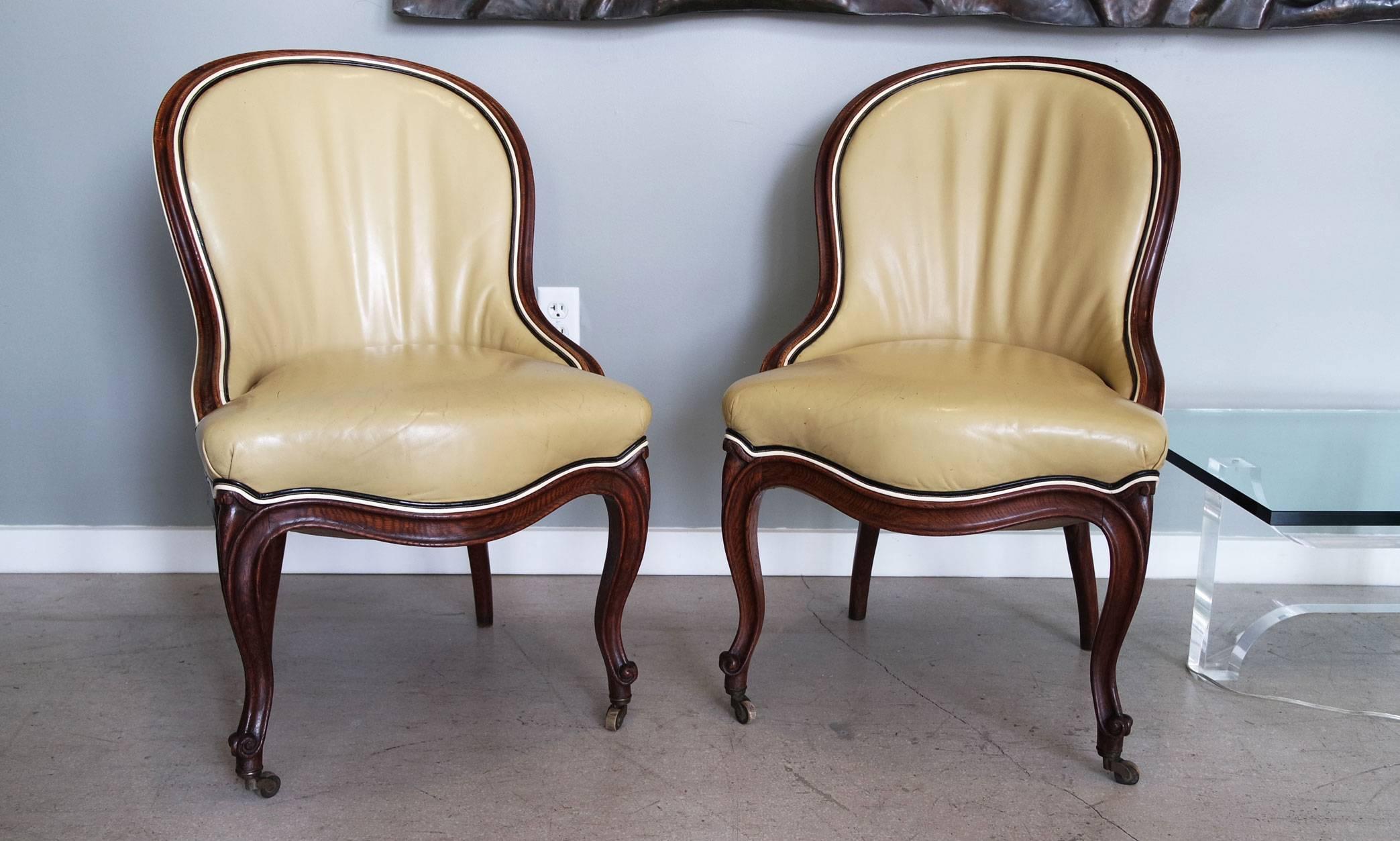 Pair of 19th century dark carved oak chairs upholstered in camel leather and piped in white and black leather. John Dickinson specifically purchased these chairs for his San Francisco fire house. One chair features a fabric tag signed, 
