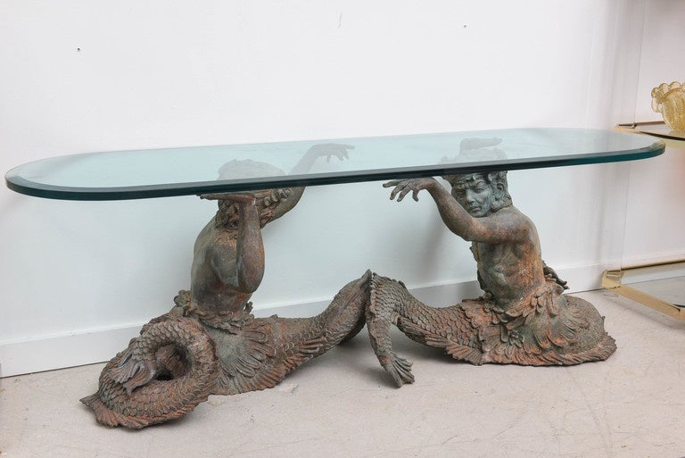 Sculptural bronze merman coffee table with an elongated oval glass top.