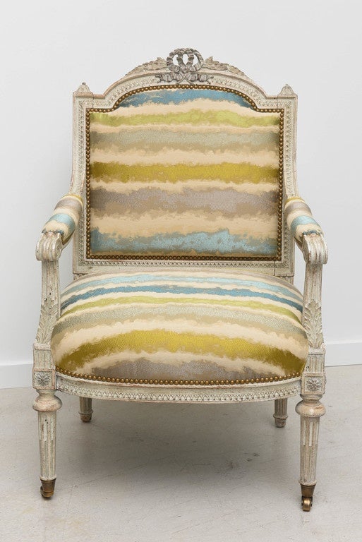 Pair of Louis XVI style painted armchairs reupholstered in multicolored stripe fabric with tones of blue green and grey. The front legs have small brass casters.