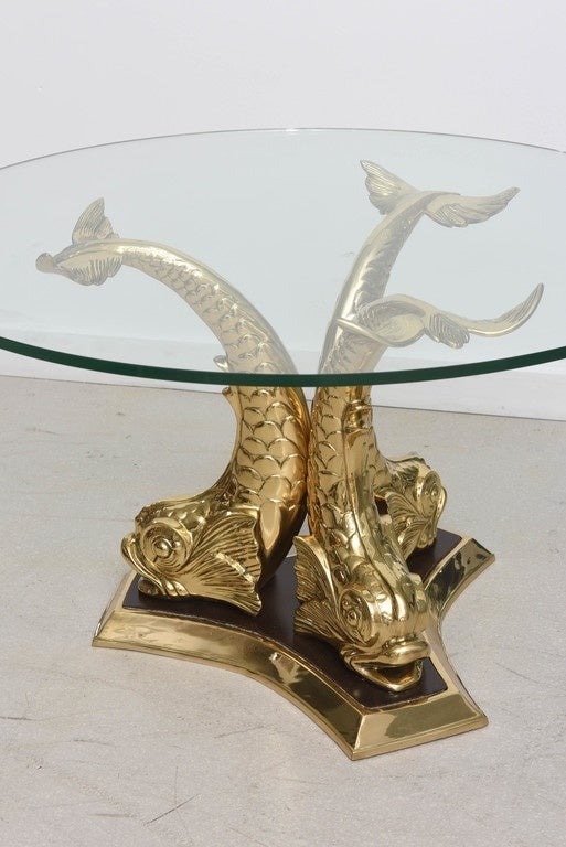 Polished brass koi fish coffee table with black accents to the base as well as a round glass top.