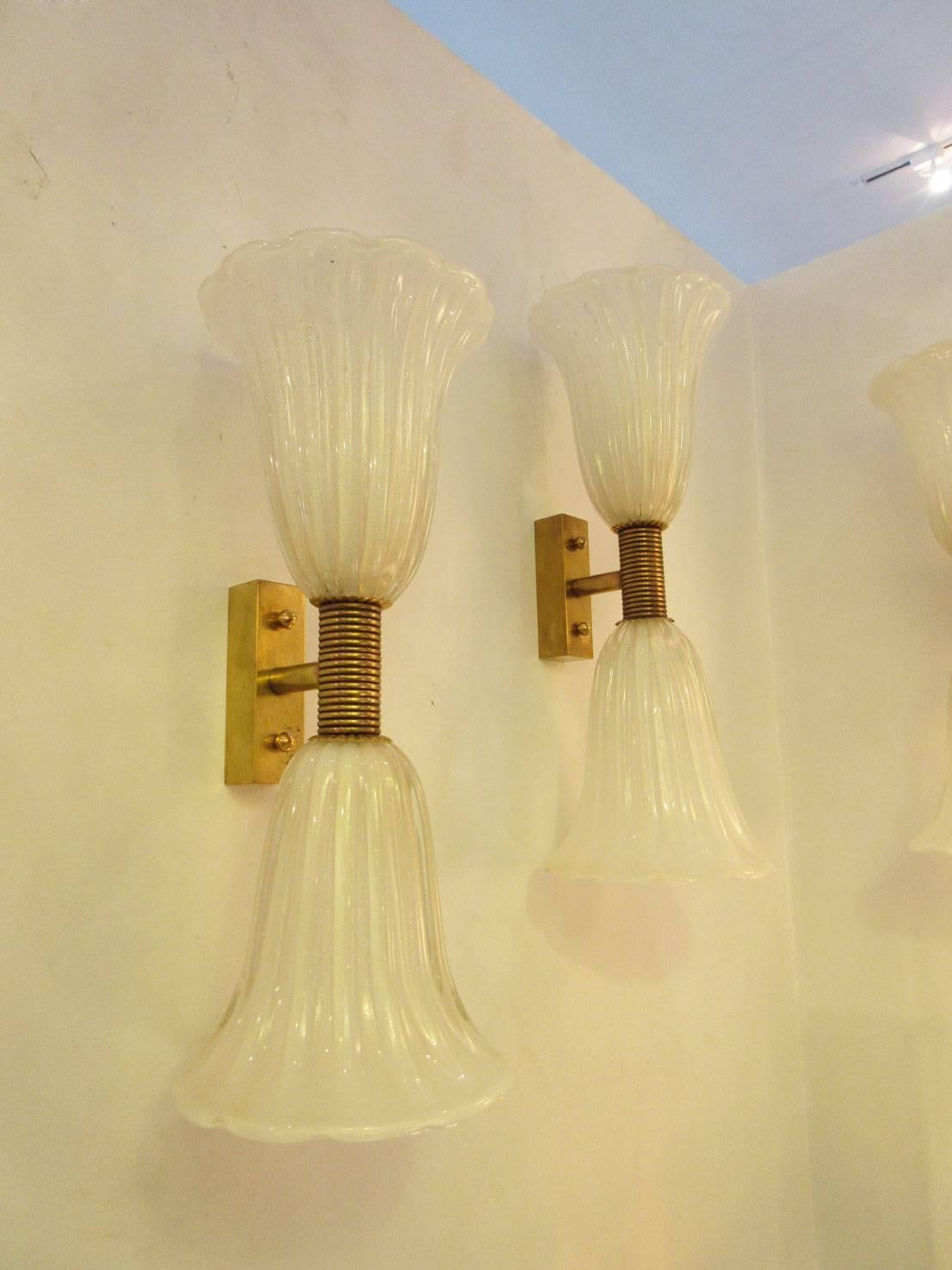 Pair of white Murano glass sconces with gold inclusions in a 'trumpet' style. Each end features a candelabra socket. The center detail is banded brass. Two pair available. They have been professionally rewired to US standards.