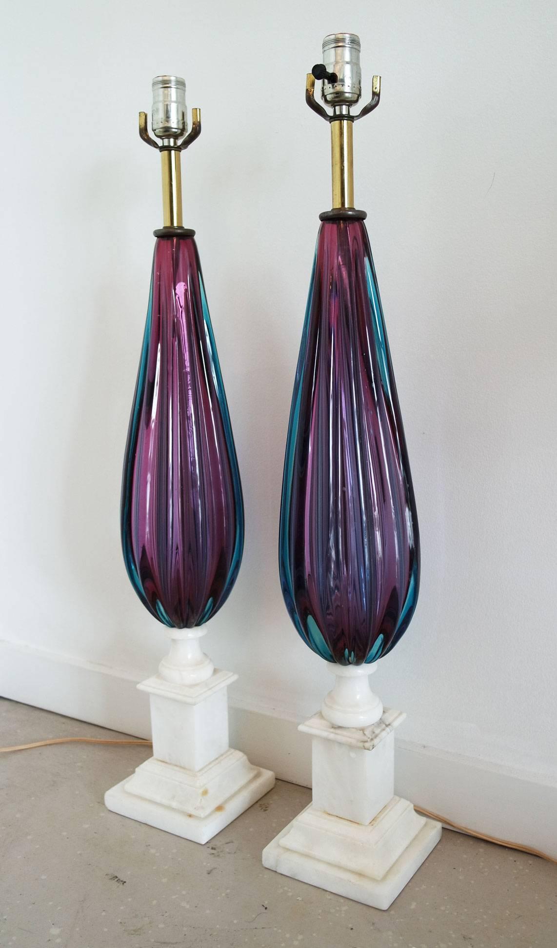 Pair of large purple and teal Murano glass lamps on white marble bases. The bases do have some chips to them, and one lamp has stress crack where the wire exits the base. They are small defects that do not distract from the overall appearance.
 