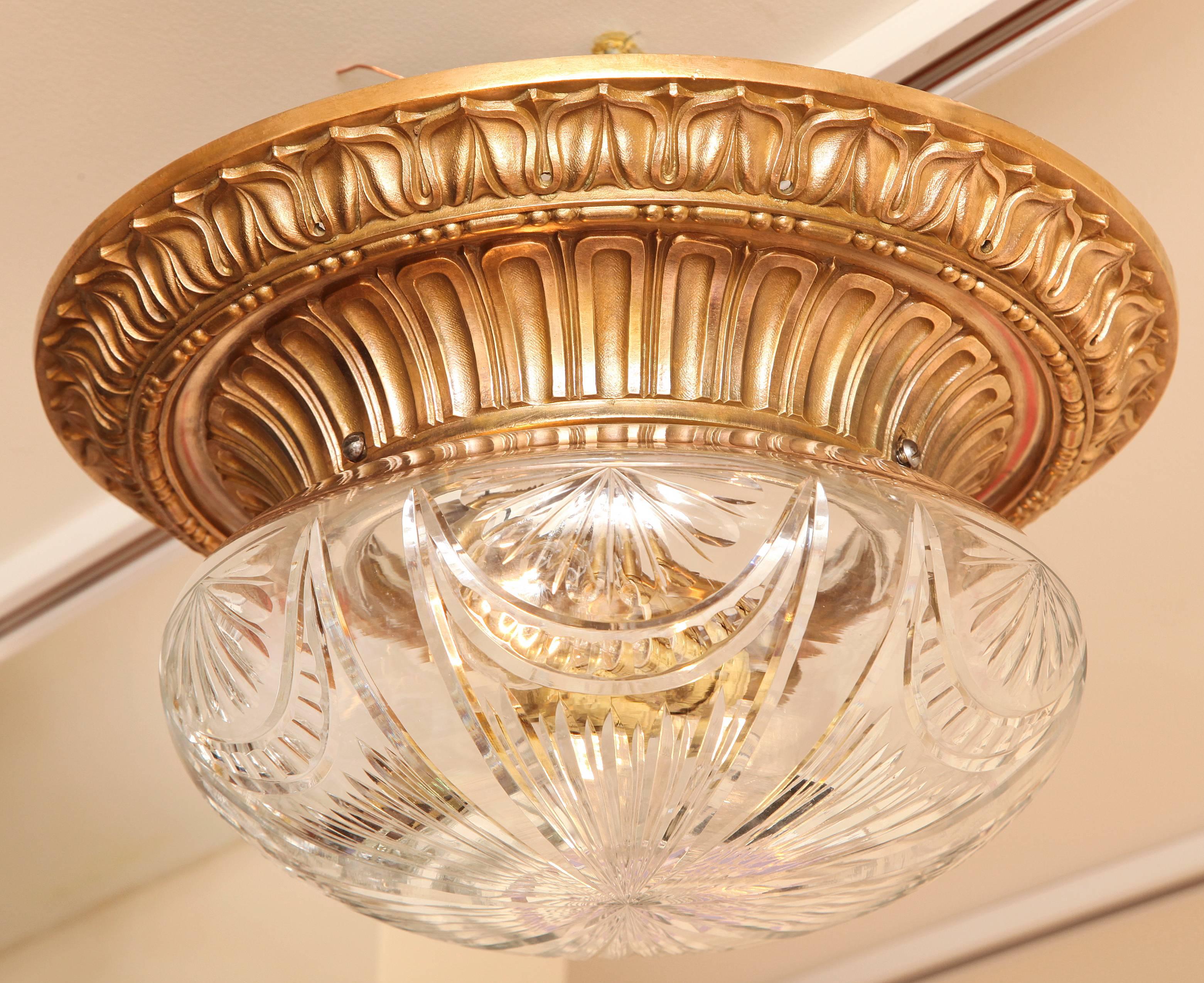 An American bronze flush mounted fixture by maker Caldwell. The round frame with leaf tip border surrounding arch fluted inner rim securing dome shaped cut-glass shade with radically symmetrical curved lines pattern concealing two Edison sockets.