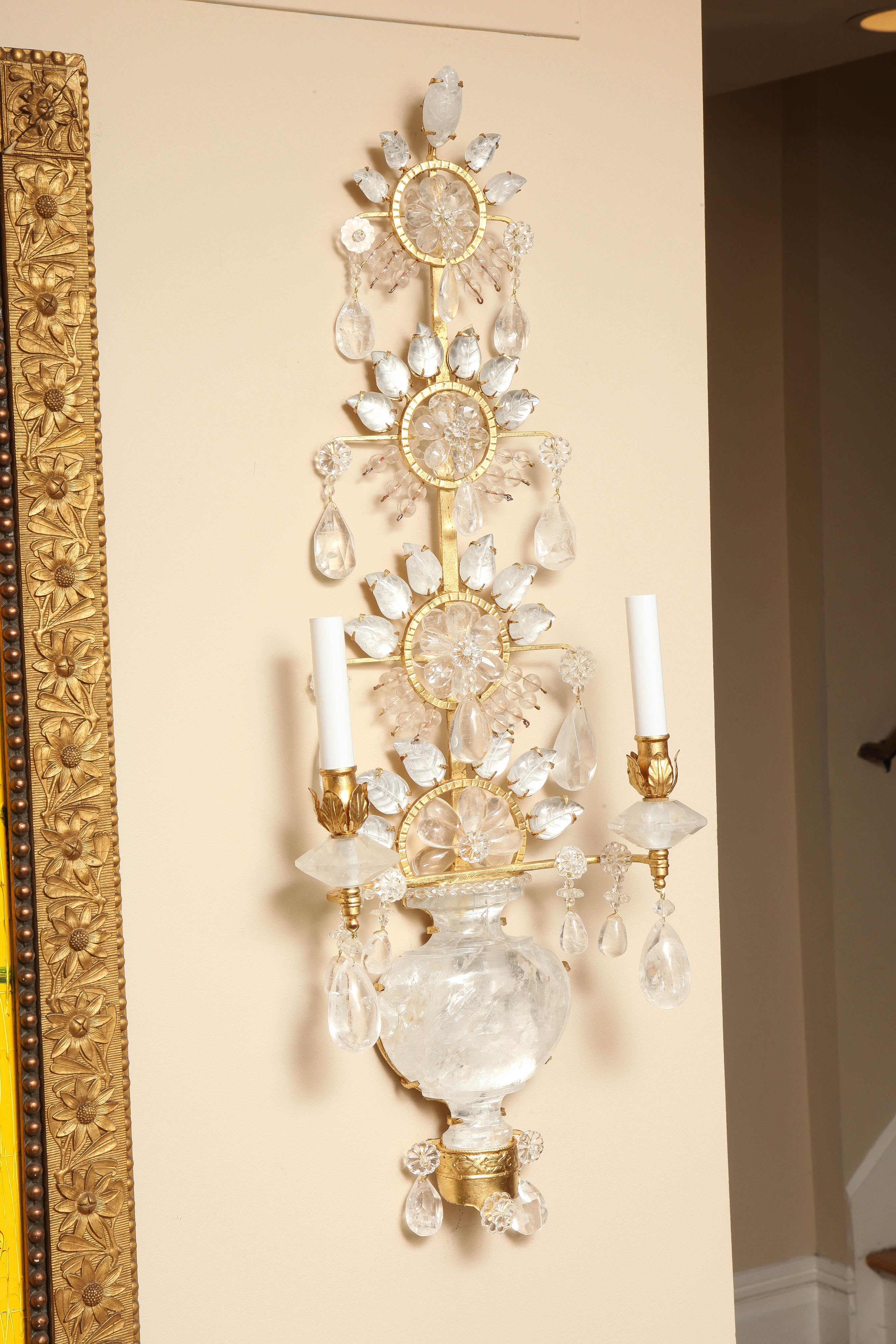 A pair of 24kt gold leaf metal two light sconces with backplate in the form of a Chinese vase in three sections of carved rock crystal. The upper section continuing into three rows of oversized rosettes formed by rock crystal beads encircled by