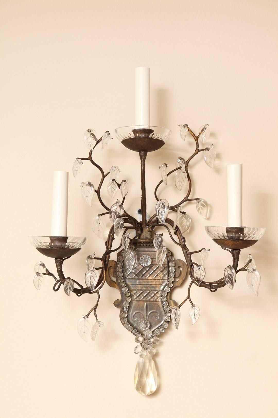 A pair of three-light French Bagues wall sconces with urn shaped back plates, having etched and cut crystal face and three stylized naturalistic branches issuing from center. Each branch with individual cut crystal leaves in the signature style of