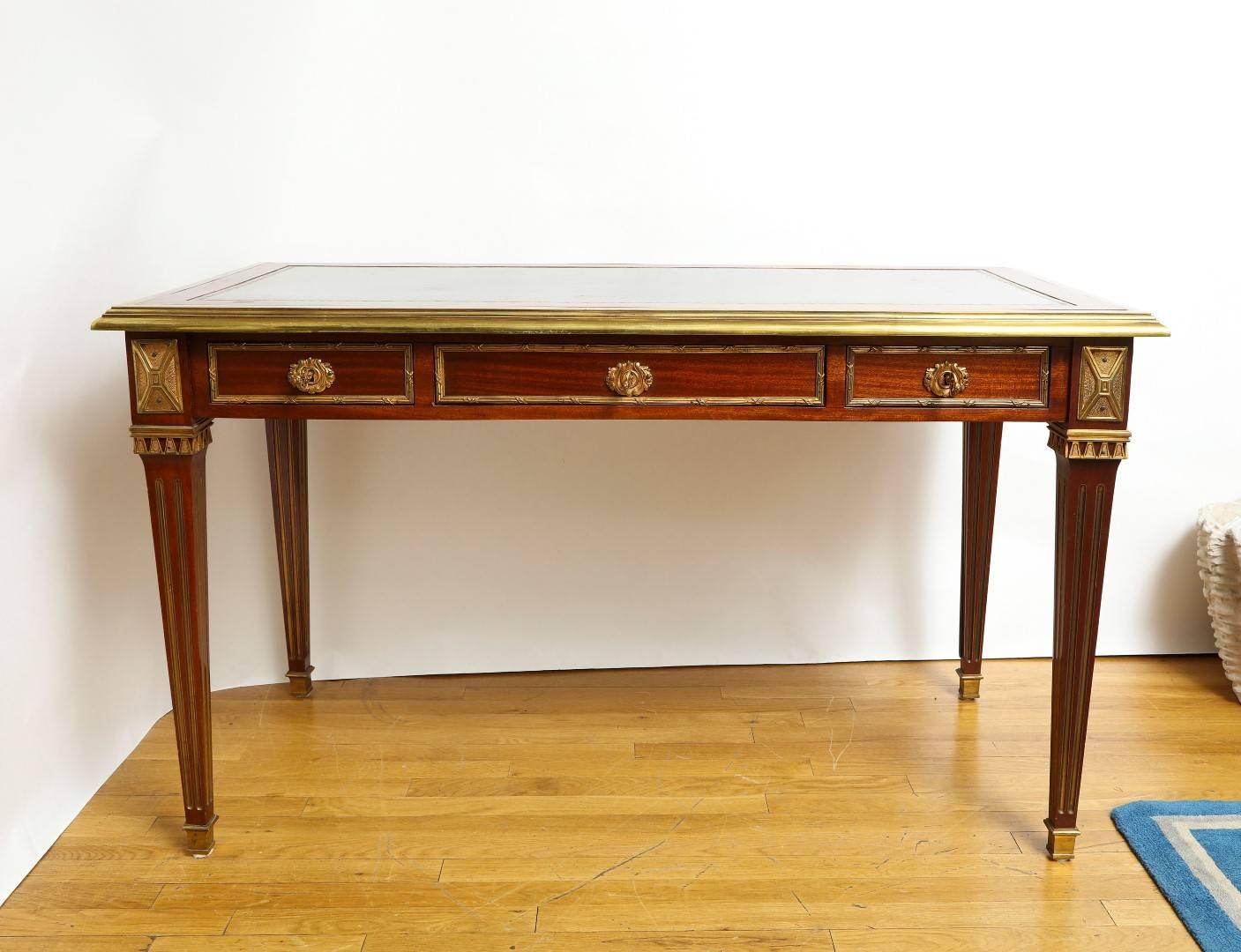 A French Louis VXI style mahogany writing table the square and tapered legs with bronze sabots and bronze mounts, the apron finished on four sides with two drawers on one side and false drawers on the opposing side. The top with bronze molded edge