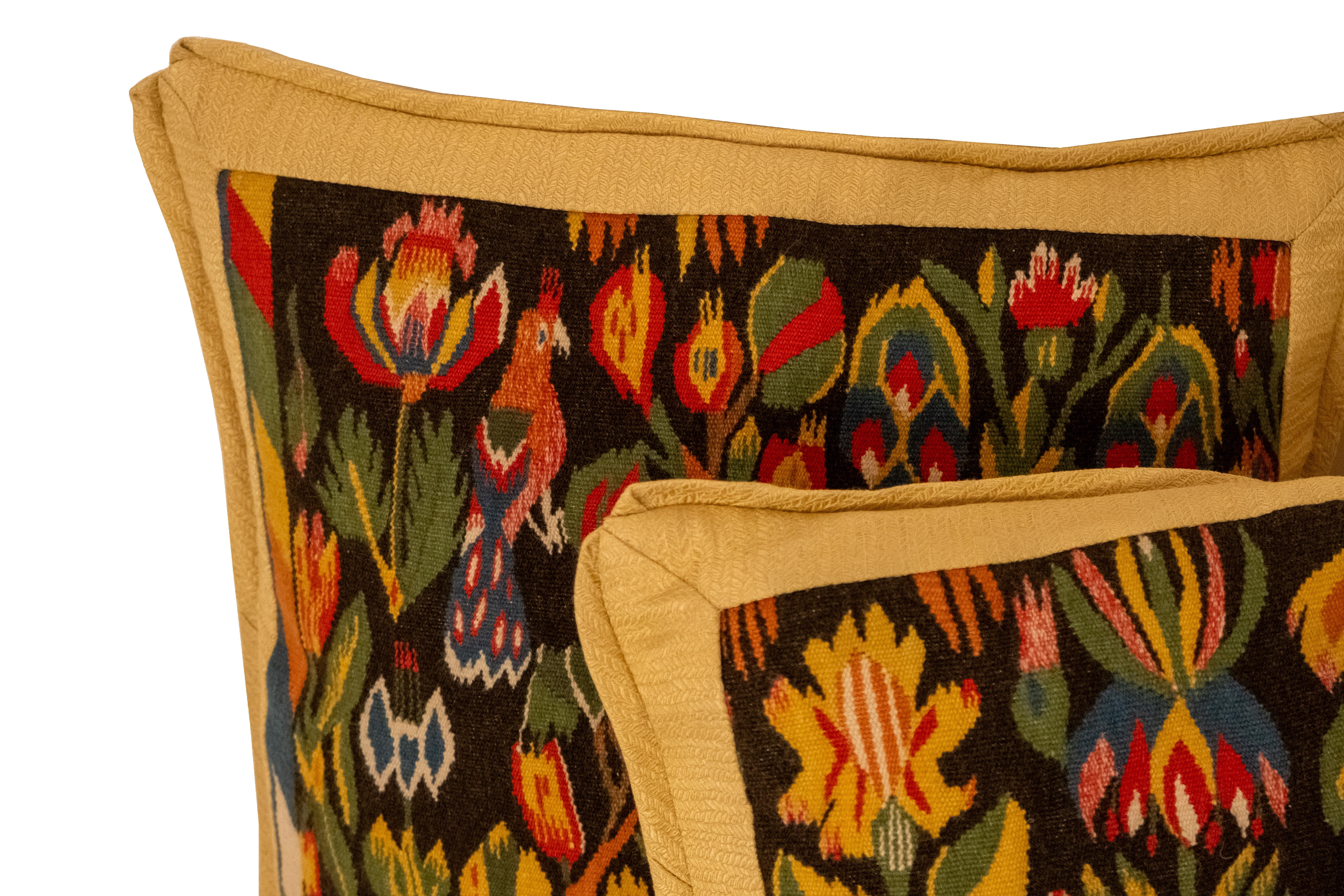 A pair of cushions made of early 20th Century Flemish-style tapestry. The colorful tapestry pieces feature a peacock and blue unicorn on one cushion, and a large parrot and flowers on the other. The trim and backs made with a Rogers & Goffigon silk