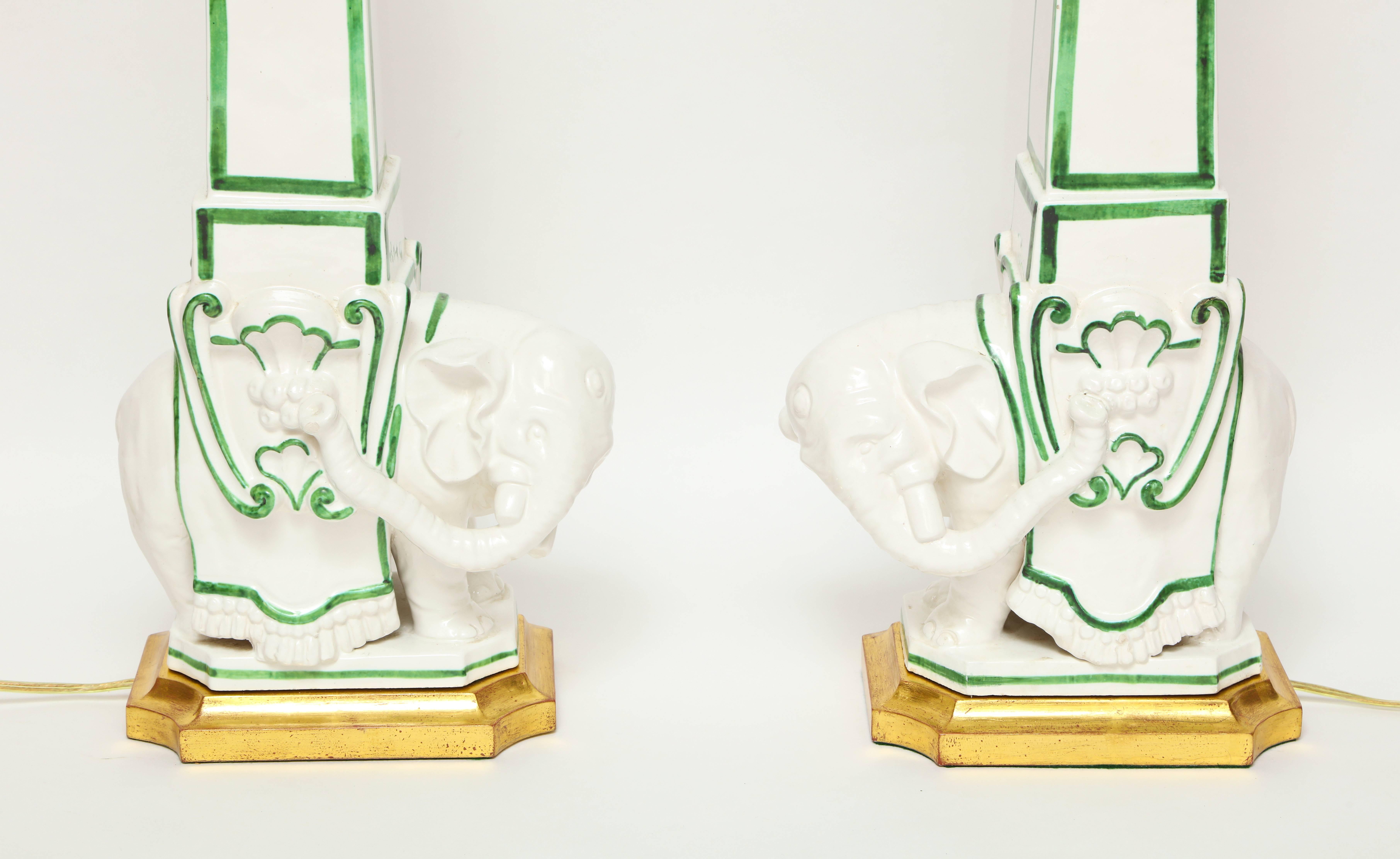 A pair of Italian ceramic table lamps, the model inspired by Bernini and his right and left facing elephants with up-swept trunks and obelisk. The white porcelain finish is decorated with green striping on each lamp with original artichoke finial