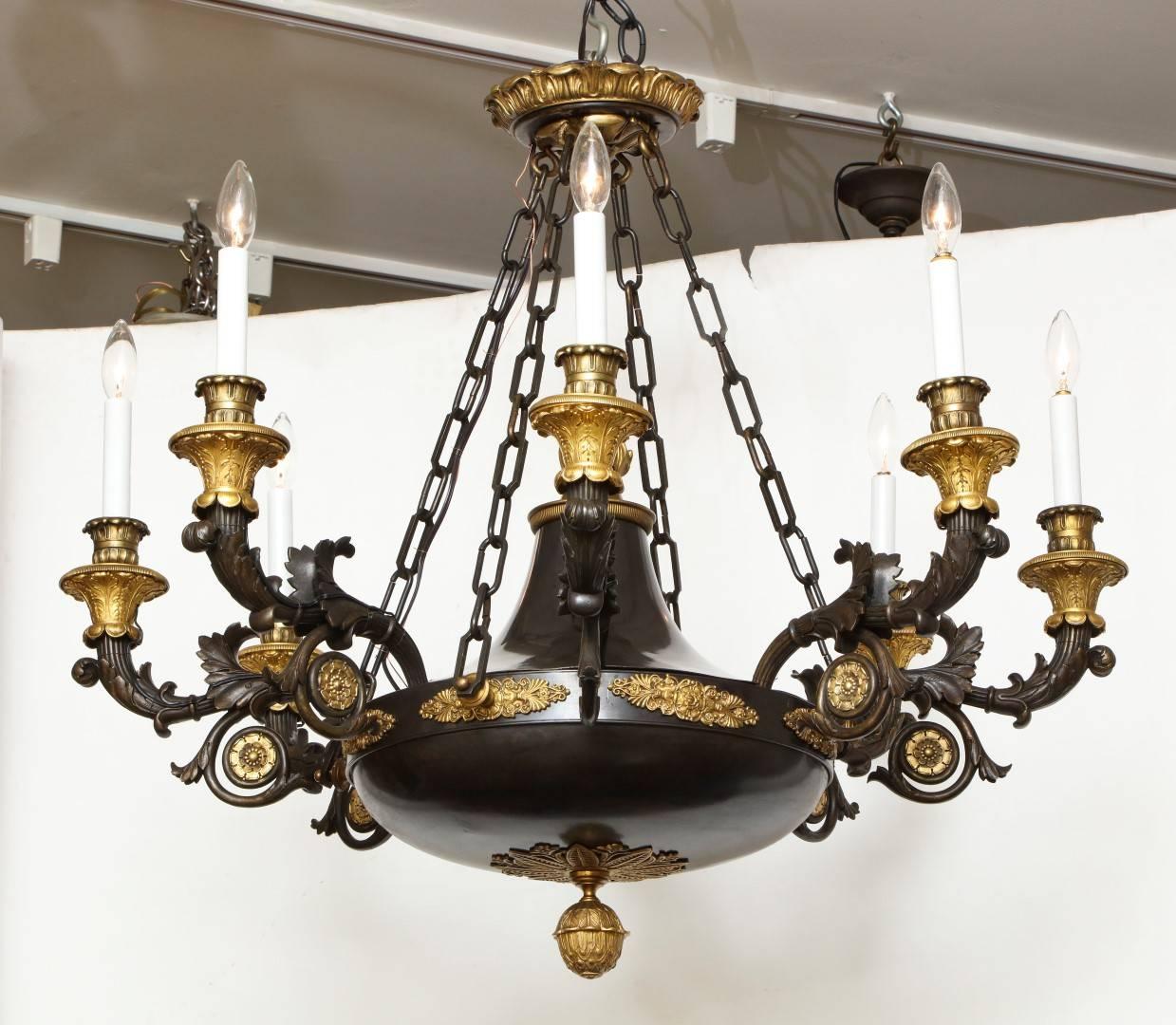 A French Empire patinated bronze and gold doré eight-light chandelier, the vase form body with flame finial and dish shaped underside suspended from four lengths of bronze chain, the anthemion mounted body issuing eight foliate scroll branches with
