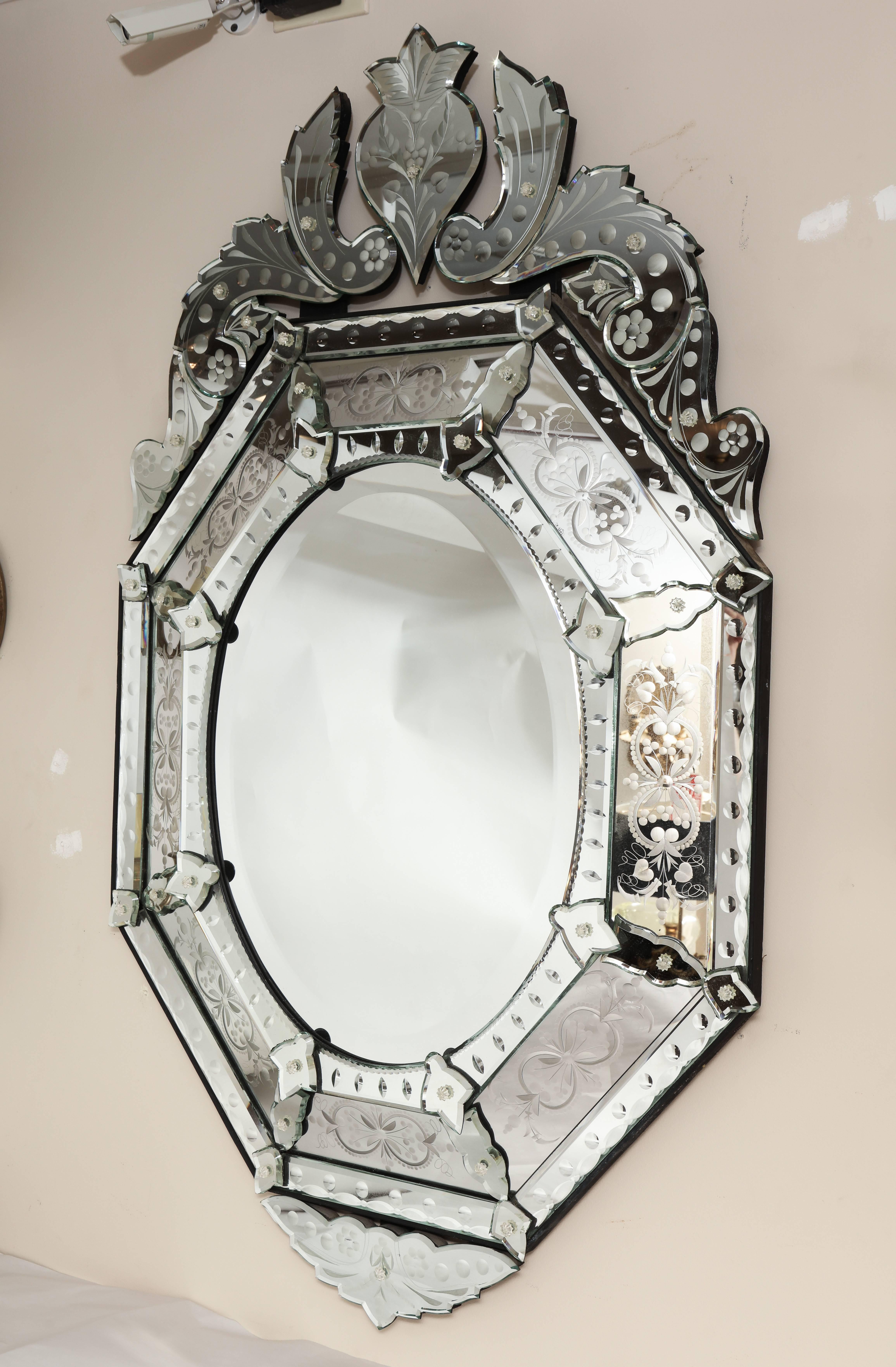 A Venetian etched-glass mirror, scroll form and leafy spray cartouche, the central oval beveled glass having mirrored outer frame with reversed glass etching and carving, each section of molding secured by mirrored rosettes.