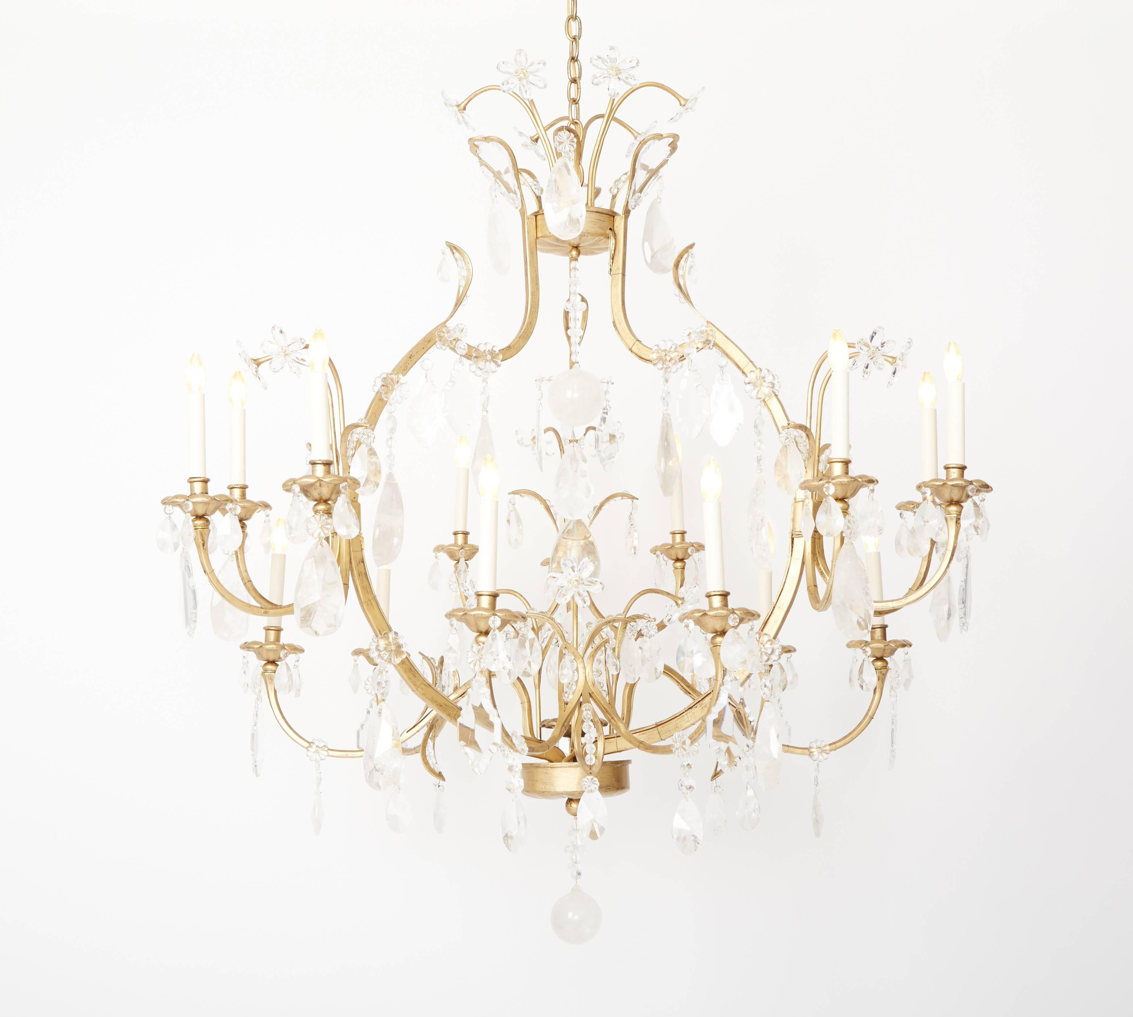 Lampadario personalizzato a 15 luci in ottone dorato a forma di gabbia in stile Luigi XV, con bracci di altezza sfalsata che si dipartono da una struttura drappeggiata con cristallo di rocca e gocce di cristallo sfaccettato. Il centro è composto da