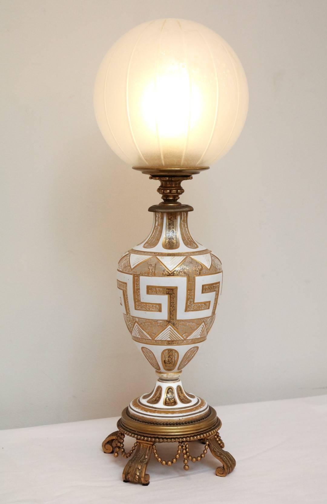 A Beaux Arts bronze mounted vase fitted as a lamp, baluster form body with oversized Greek fret motif, the waisted spreading socle resting on a stepped bronze base issuing three corbel form feet and draped beading, with removable glass