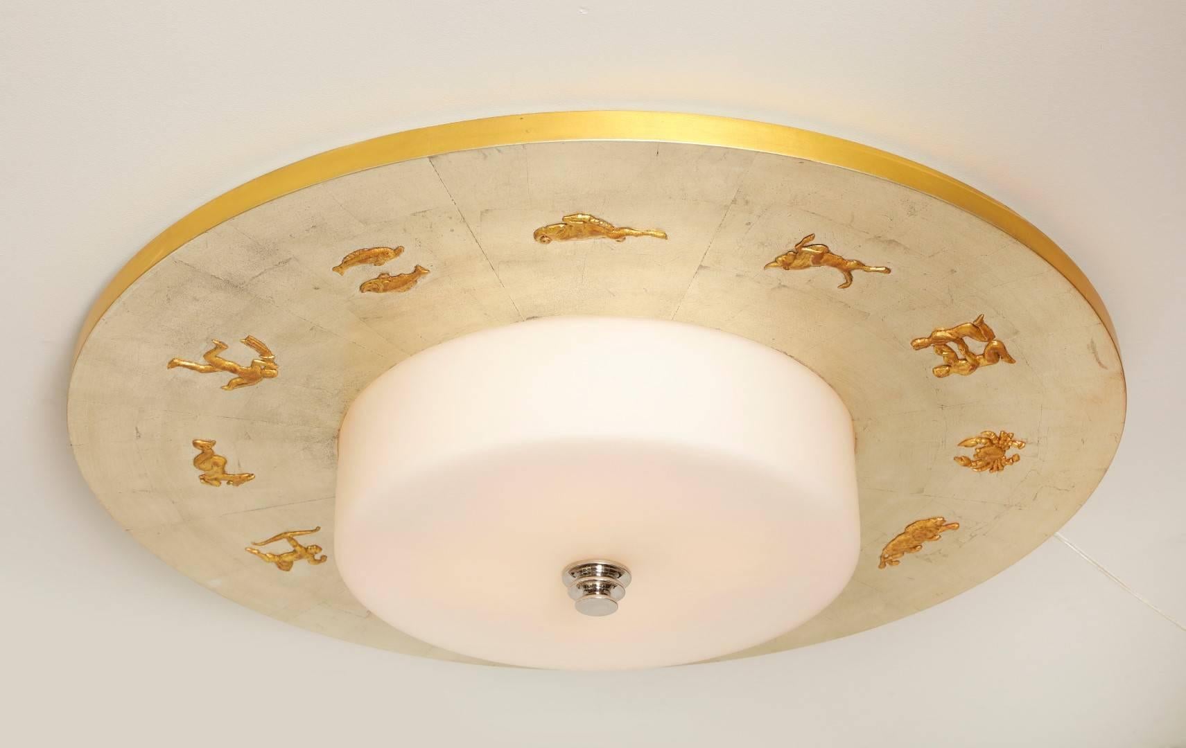 A Swedish Grace period inspired round ceiling light with disk shaped wooden frame having a white gold leaf finish, the underside encircled by low relief signs of the zodiac, the center with 16