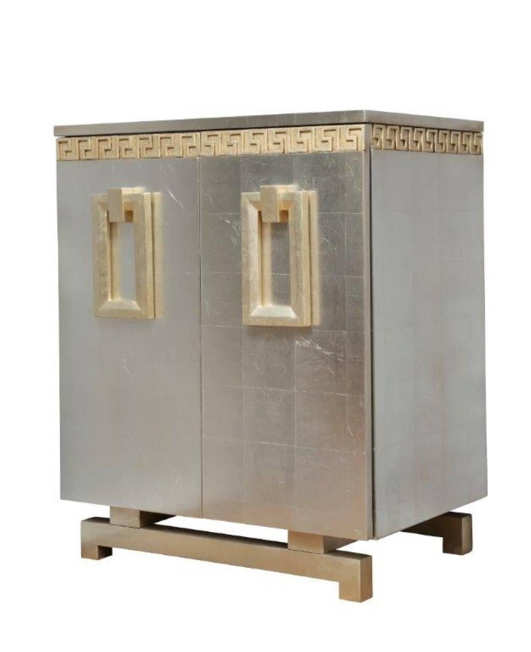 A pair of newly made Art Deco style two-door cabinets with oversized beveled rectangular ring pulls resting on open fret base, the upper section with running Greek blind fret frieze below straight edge top, the front, sides and top with silver leaf