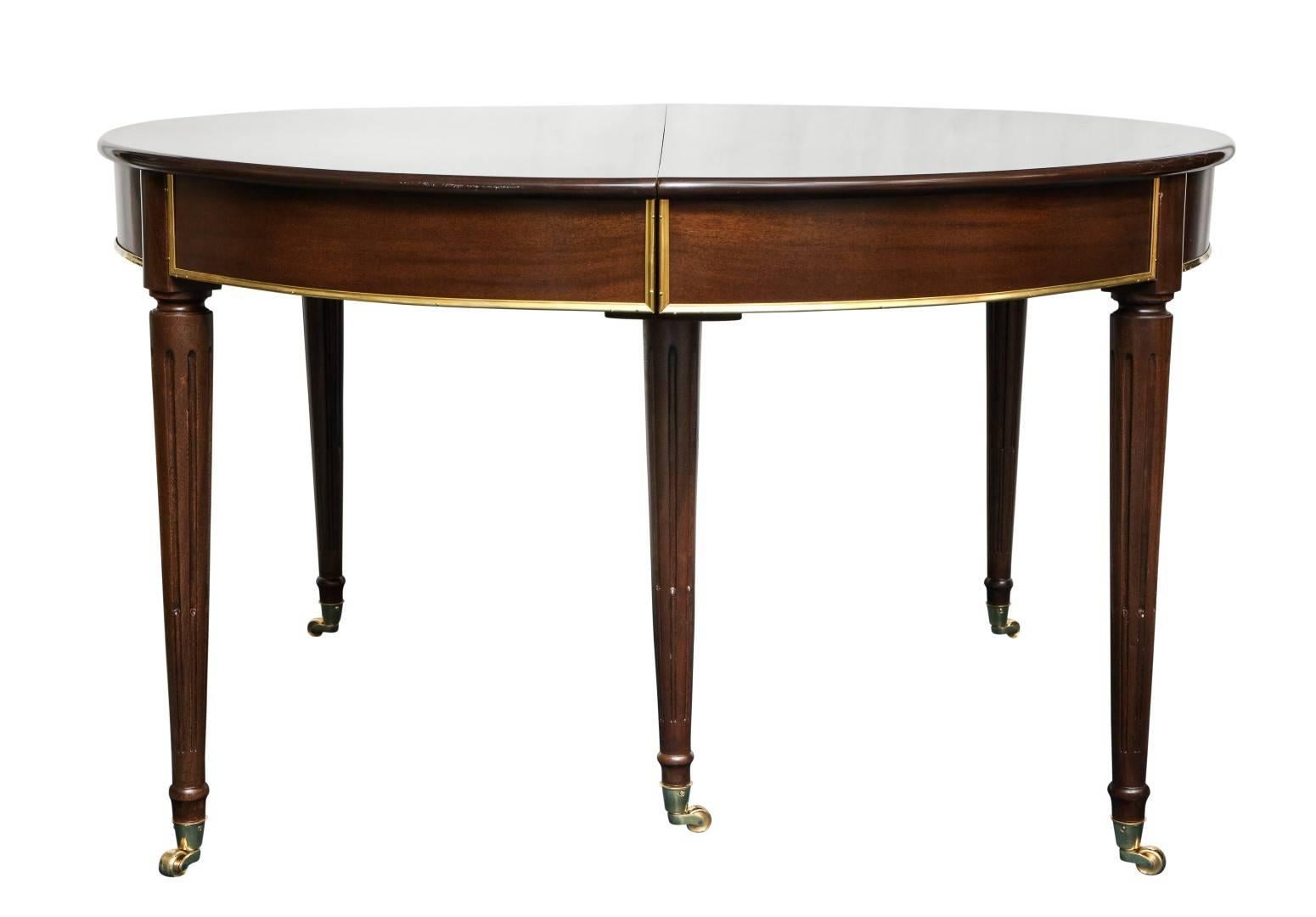 A Louis XVI style mahogany dining table, originally two semi-oval sections, four newly constructed leaves added, each stop fluted tapering leg capped with new brass collar and terminating in brass castors, additional brass on wood detail on apron,