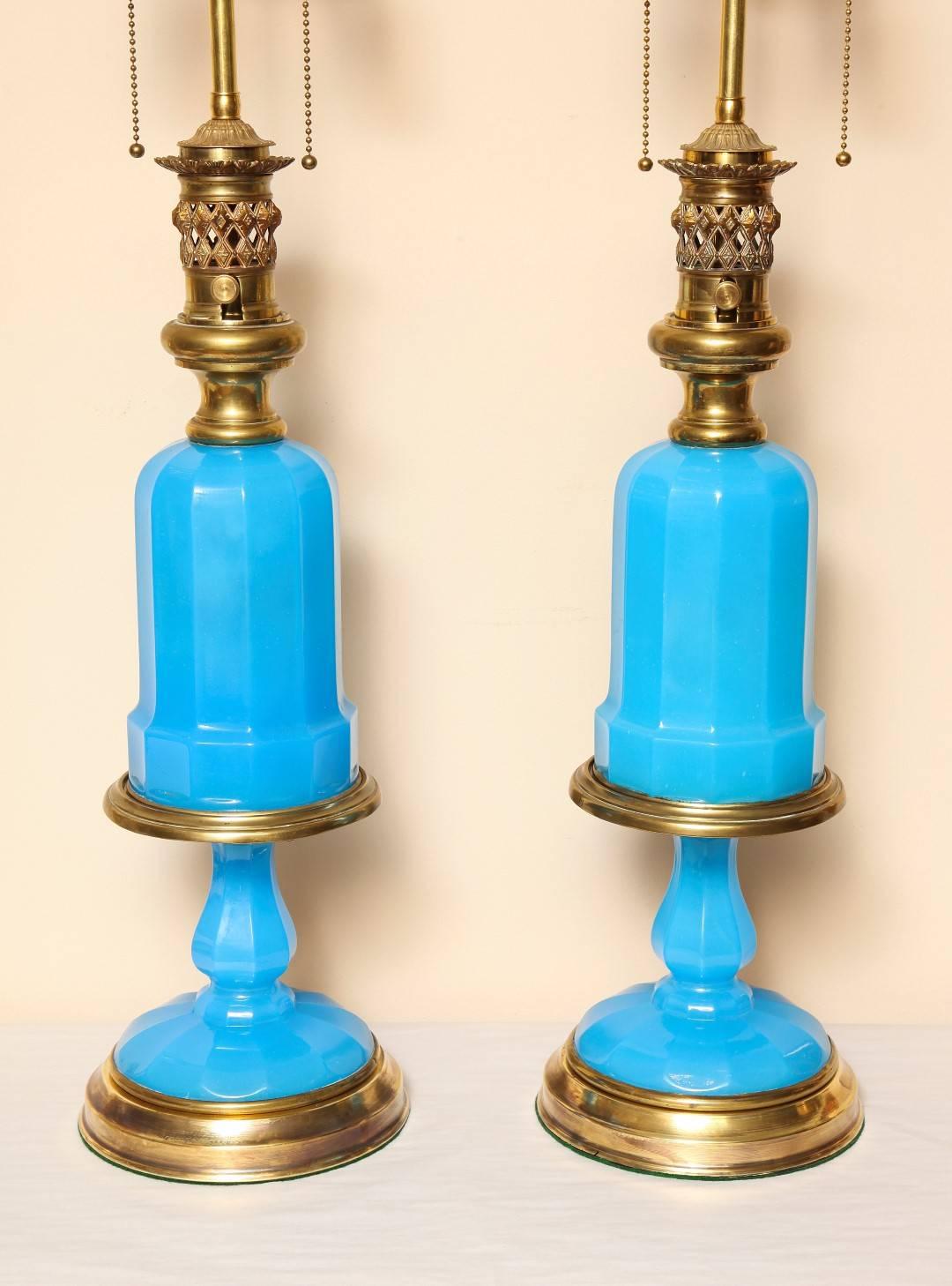 A pair of French oil lamps on stands, the opaline glass body with original brass oil fittings resting on brass and opaline glass bases, now electrified with double cluster.

30
