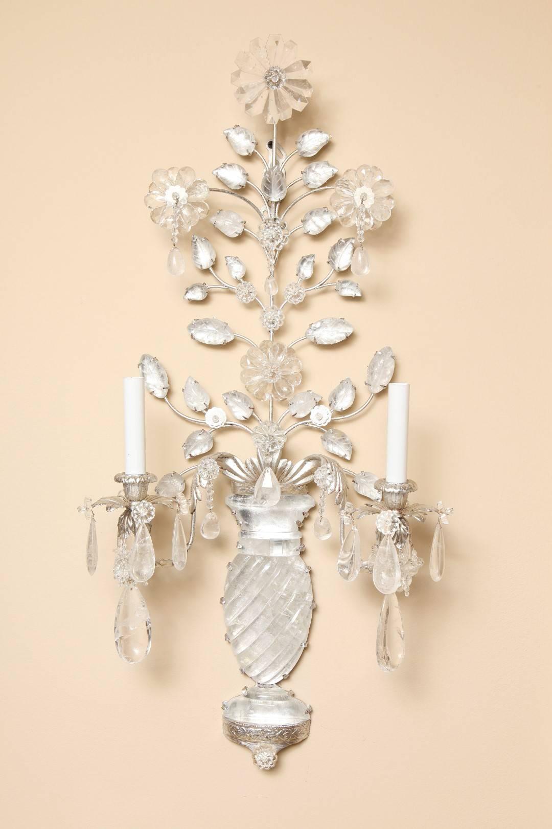 A pair of new two-light rock crystal sconces with silver metal frames, the vase-shaped back plates with spiral fluting issuing silver leafed metal branches of rock crystal leaves and flowers formed with rock crystal drops, the bobèches also draped