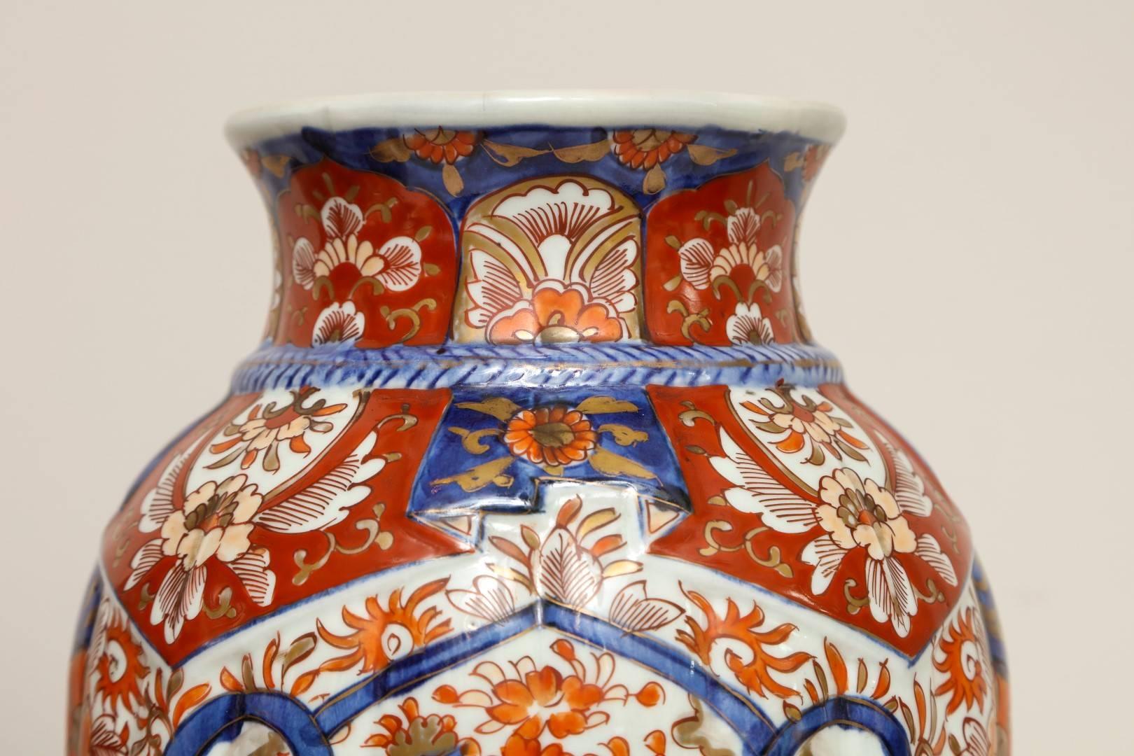 A pair of Japanese Imari porcelain vases, ovoid shape decorated in white ground with gilt highlights and shaped panels in blue and red, motif of blossoming flowers, birds and chrysanthemums.