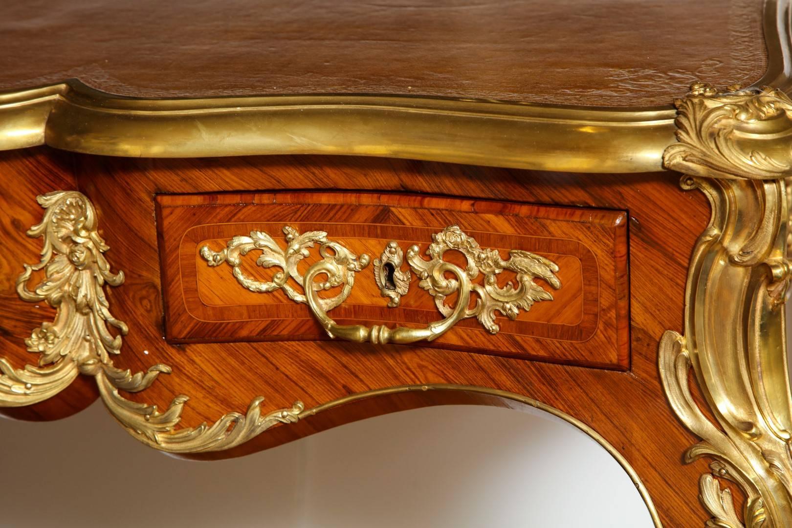 A French ormolu-mounted tulipwood parquetry bureau plat, rectangular ormolu moulded top with gilt-tooled camel leather writing surface above a shaped frieze set with central drawer and flanking damask lined short drawers, the reverse with similar