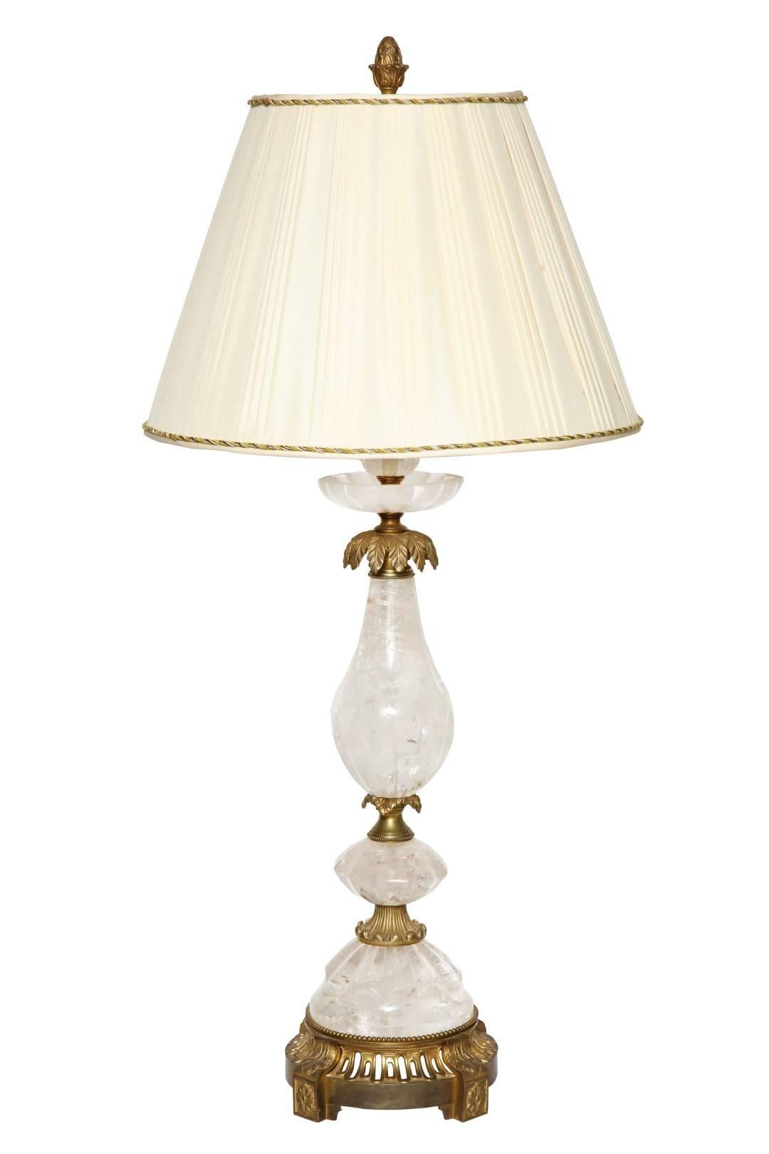 A pair of new rock crystal table lamps with antique gilt brass fittings, the palm frond collar resting on a baluster shaped rock crystal shaft, the pierced circular base resting on four corbel form supports with acanthus leaf and rosette details,