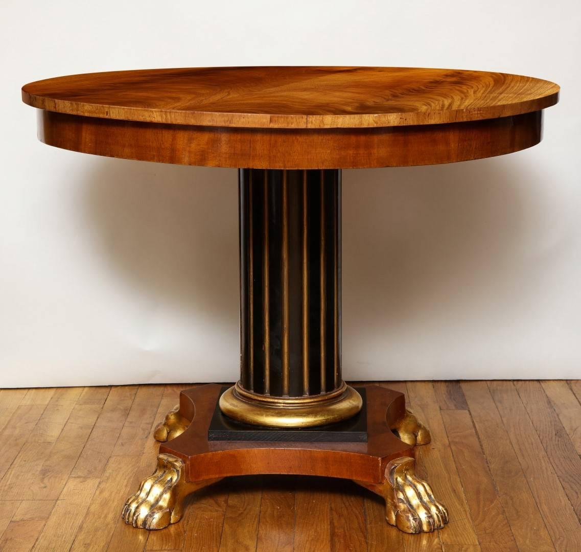 A Regency centre table, parcel gilt and ebonized fluted columnar shaft resting on an arched base with gilt paw feet, the tulipwood top with glass cover.
 