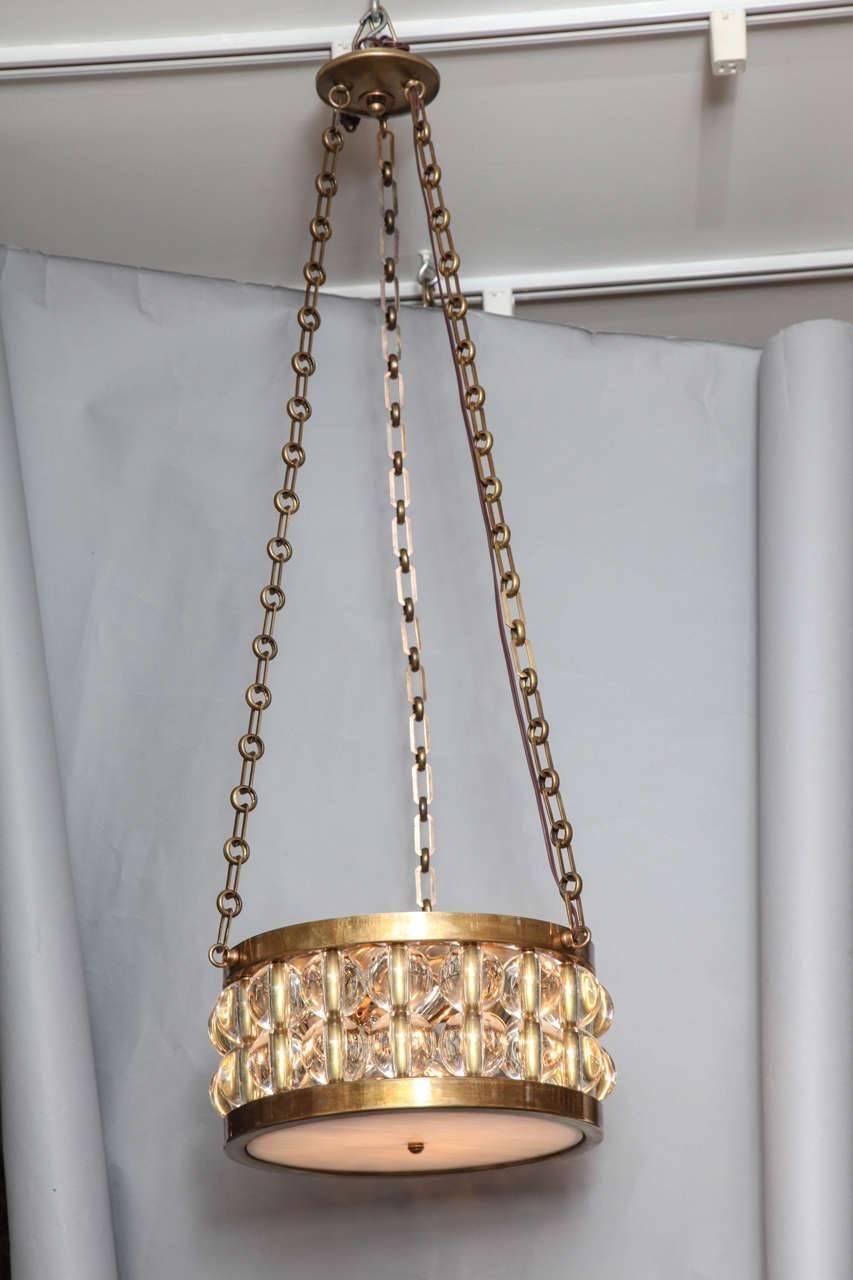 A two-tiered Tambour pendant light, the round polished patinated brass metal frame having two tiers of glass spherical elements suspended from length of bronze chain and canopy, the four light electrical fitting concealed by hand blown opalescent