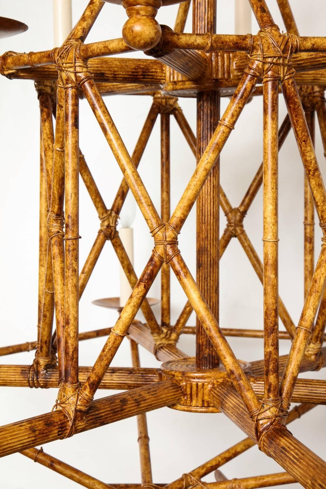 A twelve-light two-tiered cage form chandelier, with cage form by cross banded sections of faux tortoiseshell bamboo painted metal. Bobeches issuing electrified candles with maximum of 60 watts per socket.

