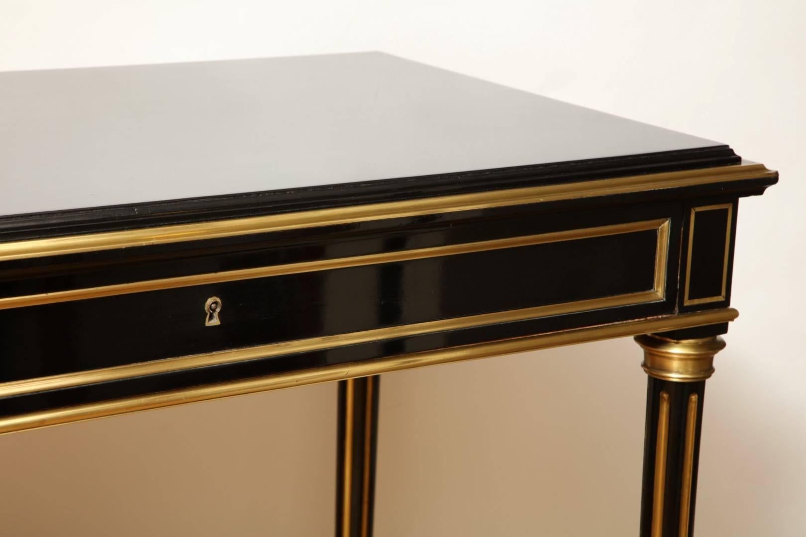 A French Directoire style ebonized desk. The ebonized mahogany frame having top with inset molded brass edge, supported by four brass fluted legs terminating in toupie feet