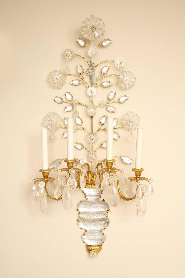 A pair of new four-light rock crystal sconces with gilt-metal frames, the vase-shaped back plates with etching motif and gadrooned waist, issuing gilt-metal branches of rock crystal leaves and flowers formed with rock crystal drops, the bobeches
