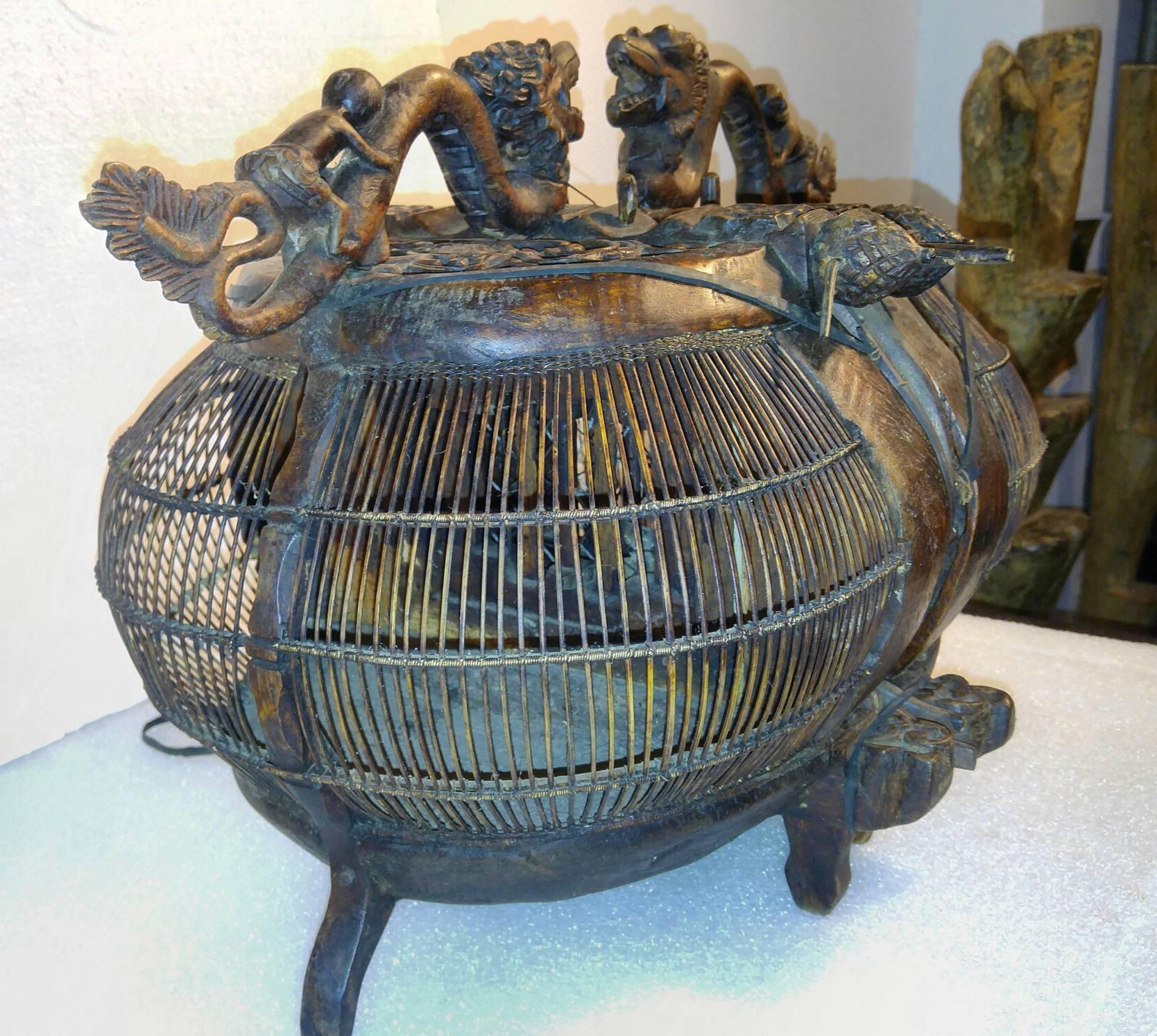 A decoratively carved wooden bird cage from Lombok, Indonesia. Twin cages with carved dragons and riders on top and floral carvings throughout.