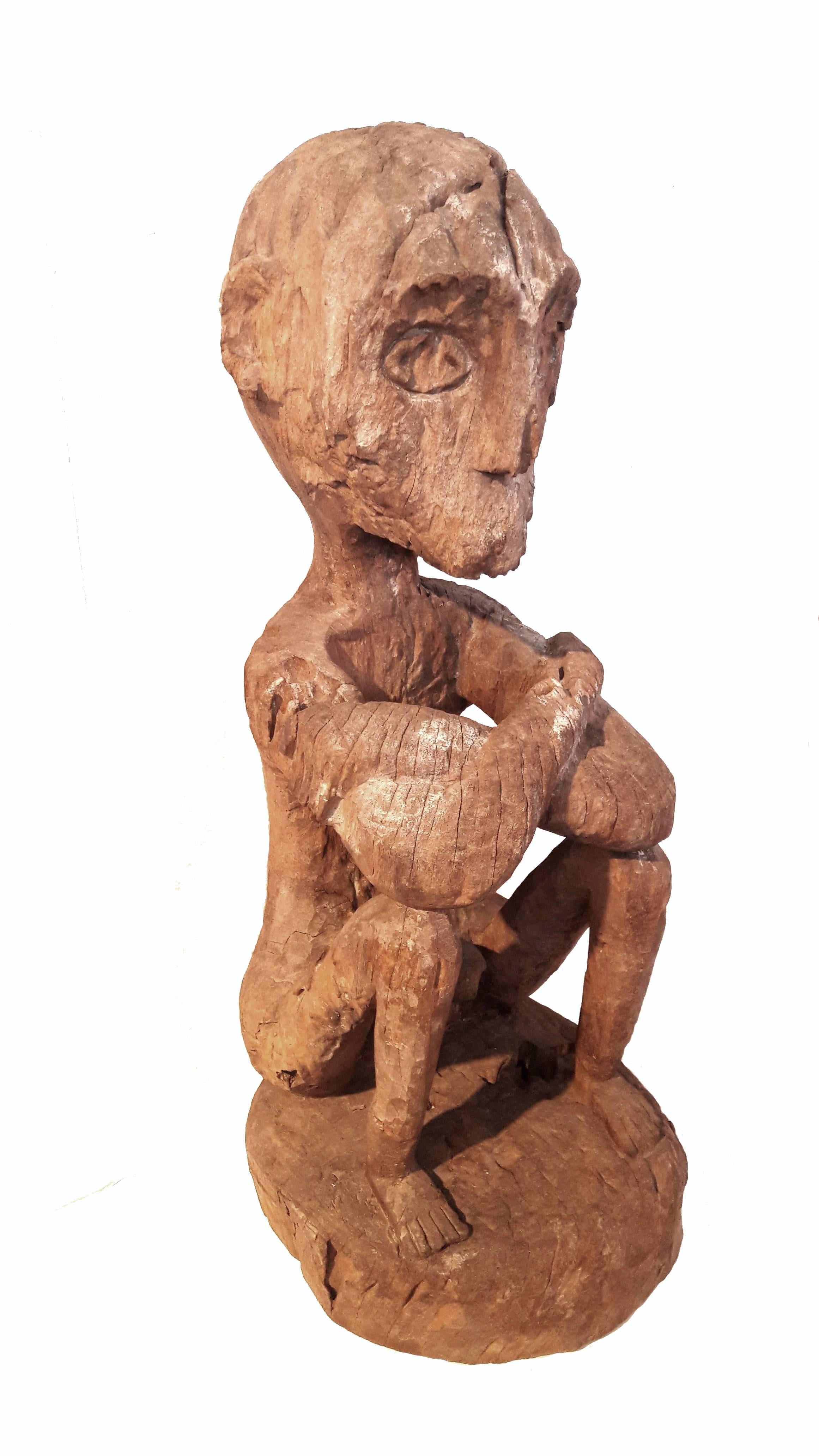 A traditional Benu'aq sculpture of a sitting man, from East Borneo. Carved from a single piece of  ironwood, circa 1920, this figure shows the erosion and patina according to its age and the distressed nature of the wood.