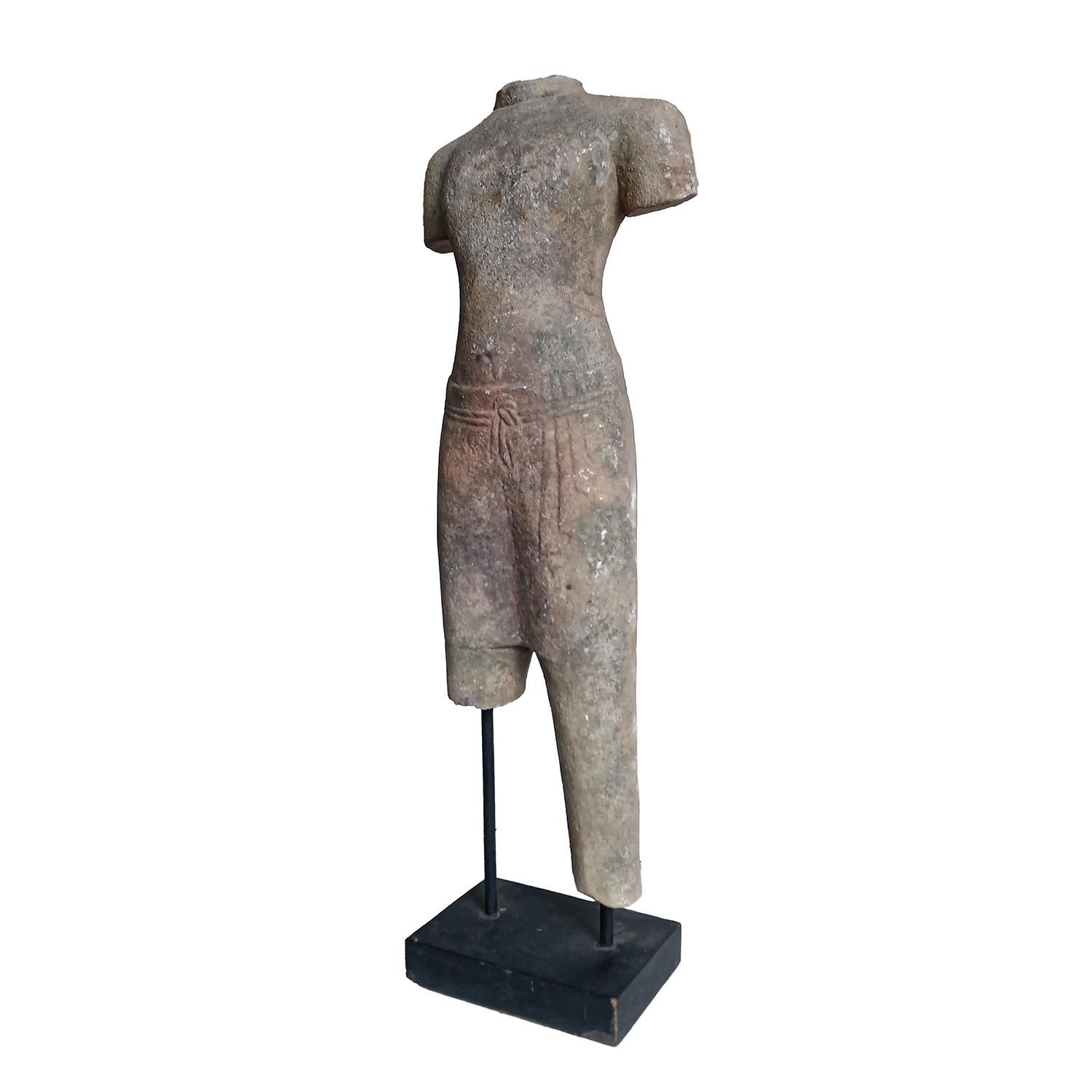 A table-top sculpture of a male torso in traditional attire, hand-carved from a single piece of weathered sandstone, preserved in its natural color. Thailand, late 1970s. 

Mounted on a wood / metal stand. 26.5 inches total height. Stand base: 9.5