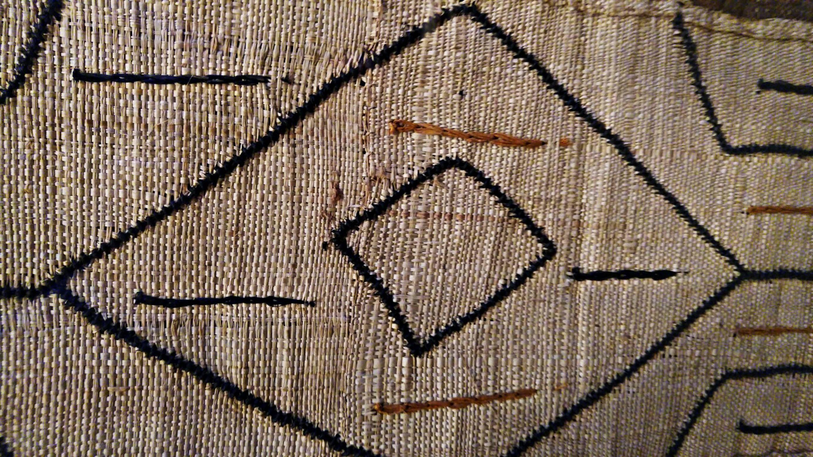 A traditional Kuba cloth depicting geometric and freestyle patterns in tan, brown and orange, from Congo, mounted in a frame with glass. Wired to hang horizontally or vertically.