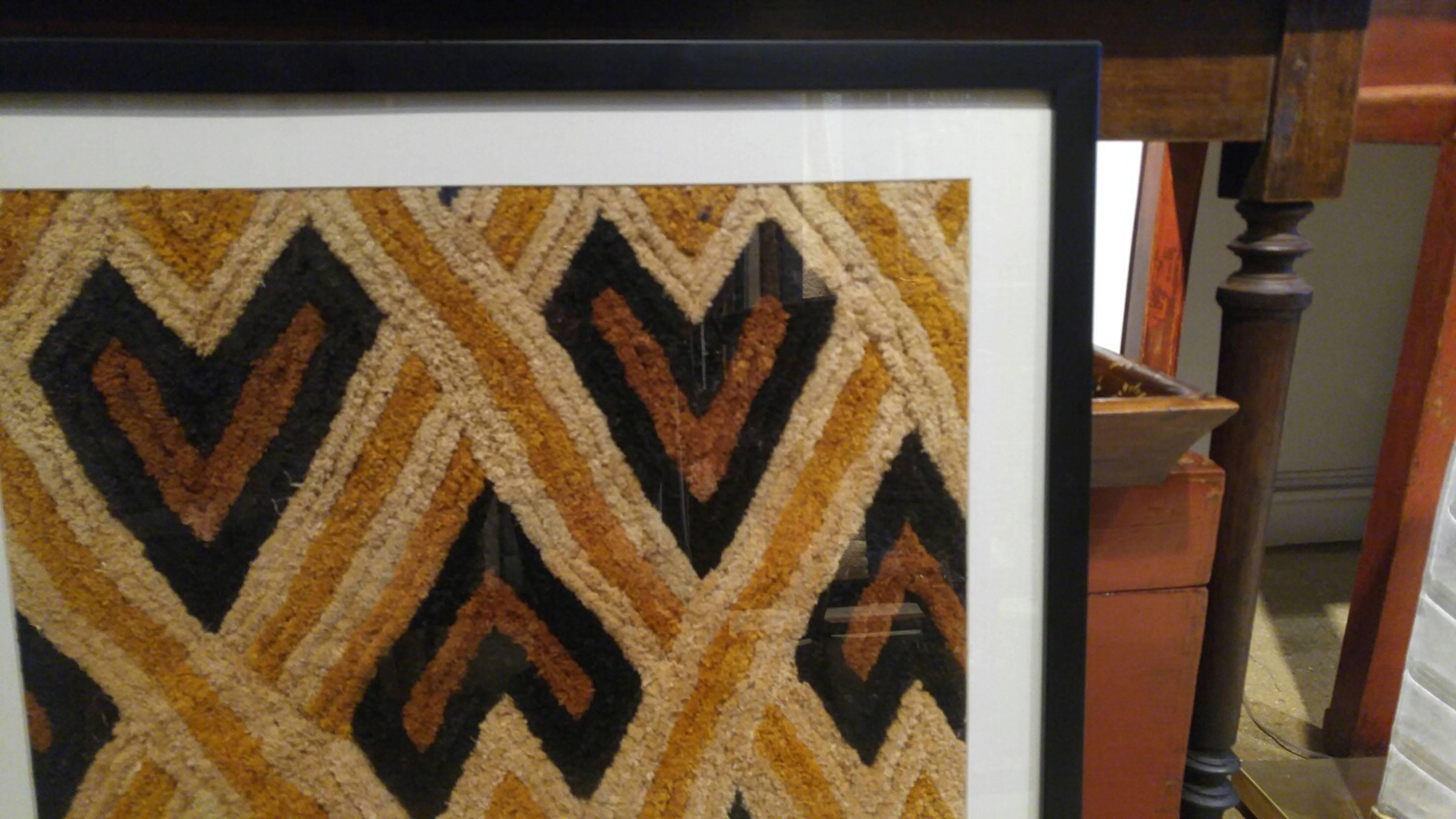 A Kuba cloth from Congo. Woven raffia in traditional geometric pattern. Mounted in a frame with glass for wall hanging. Can be hung horizontally or vertically.