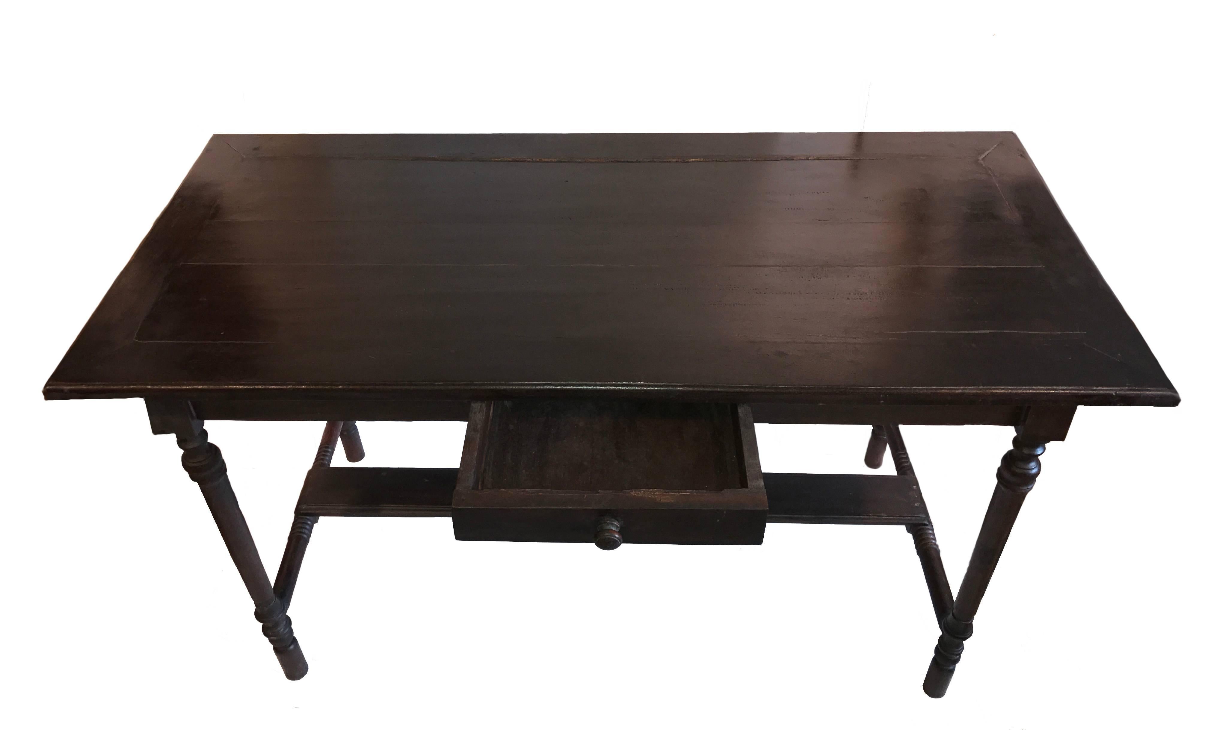 A dark wood Dutch Colonial-style desk with a single drawer, turned legs and side stretchers with footrest. This desk shows a solid, sturdy craftsmanship, while carrying the charming signs of a vintage, timeless piece of furniture.