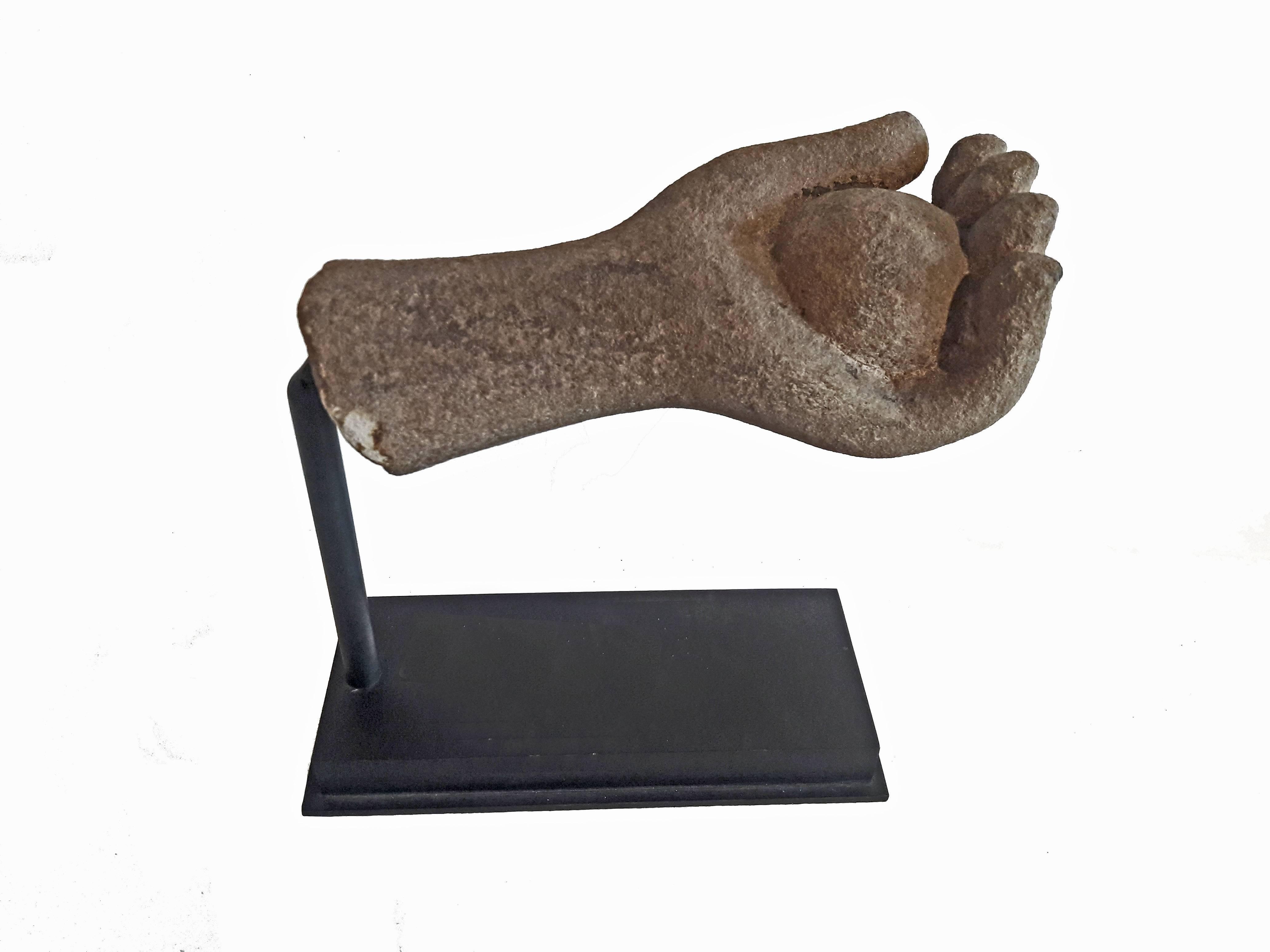 A carved sandstone Buddha hand, holding a circle. From Thailand. Mounted on a black metal stand.