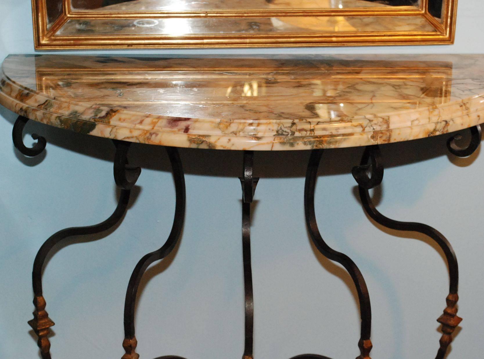 A pair of marble iron console tables. Each surmounted by an especially well figured and crossbanded breccia marble demilune top; the openwork plannished iron under frames detailed with tendril scroll and embellished with gilded knops.