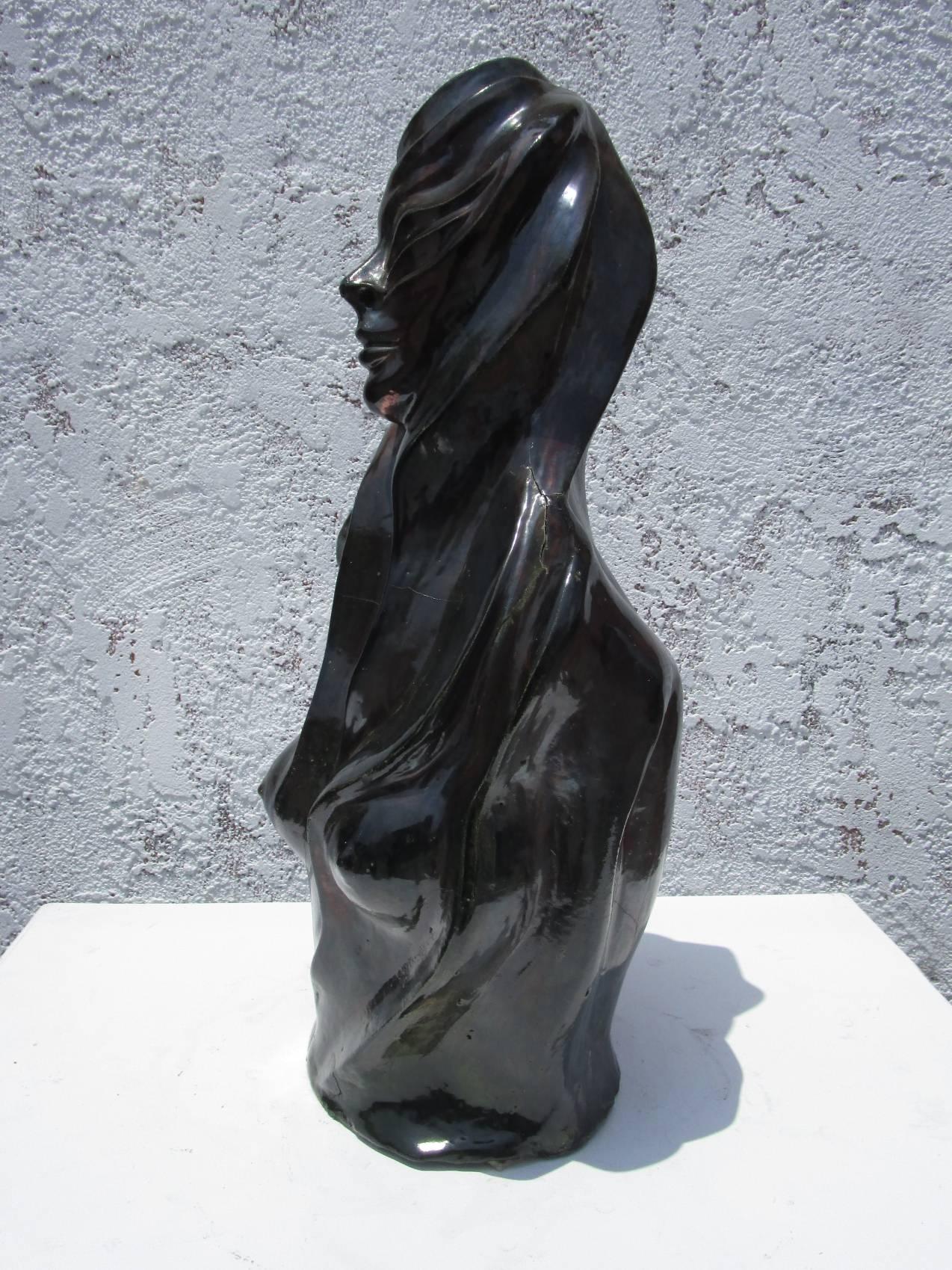 This ceramic sculpture of a nude female figure is built with angular features and a dark almost black glaze with incredible dark greens / reds / browns reflects. The depiction of the hair indicates movement and the woman has a serene expression. The