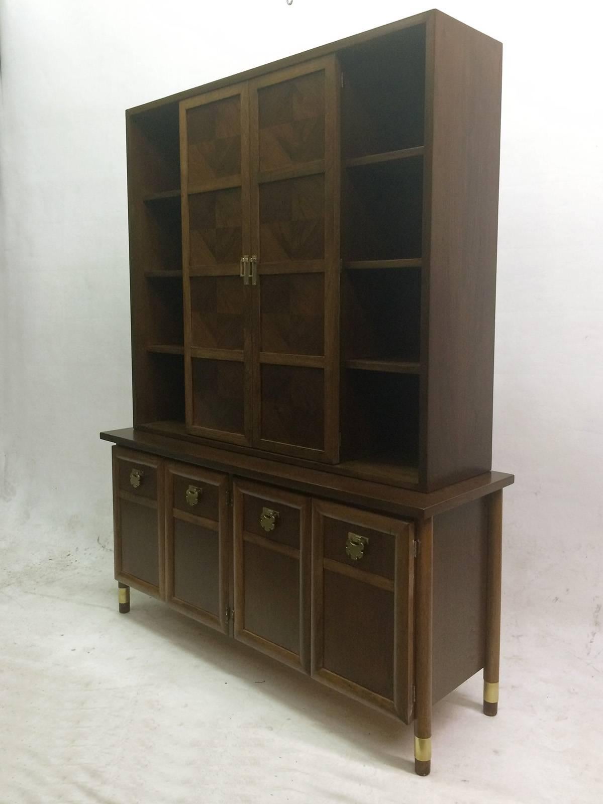 This two-tier buffet is composed of a top shelving unit and a bottom four doors cabinet. The doors handles and legs detailing are made of brass. The bottom piece has four doors - two opening to a compartment with two sections and a drop-down drawer,