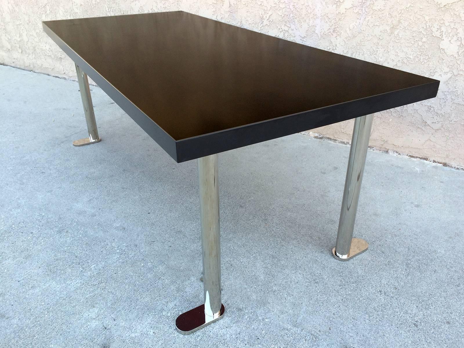 This striking black lacquered table sits upon four polished chrome legs. The tables splayed, flat feet give it a playful almost cartoonish feel. This piece may be used as a dining table and or a desk.