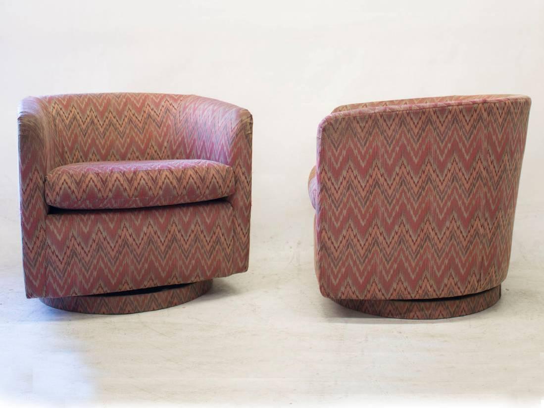 This pair of barrel back swivel chairs by Milo Baughman, have its original upholstery with a patterned fabric in a predominantly red palette.