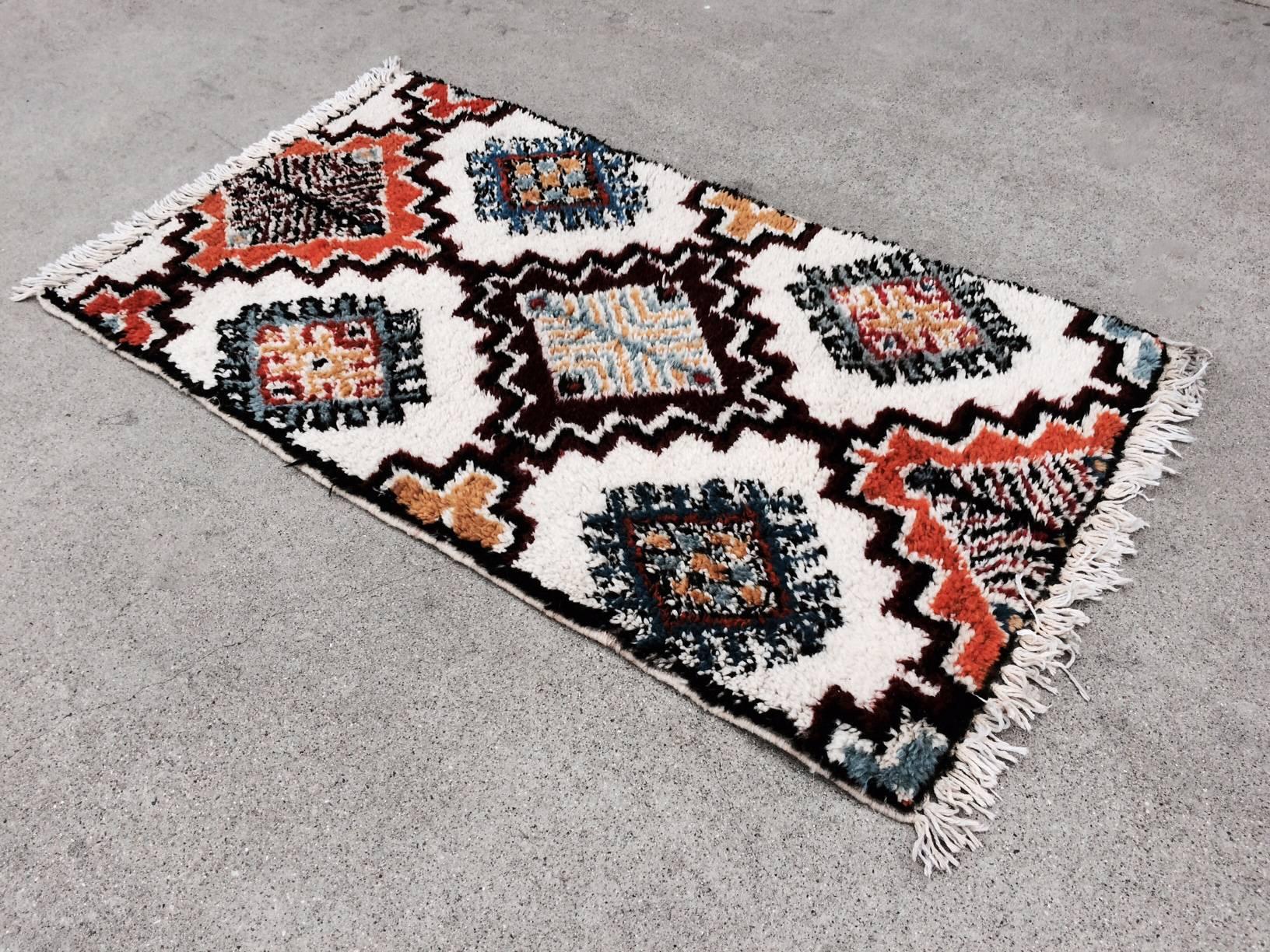 This Moroccan shag wool rug has a geometric pattern in a palette of predominately orange and blue complimentary colors and contrasting black and white line and space. The tapestry has its original tag from Rabat in Morocco. It is dated 1977.