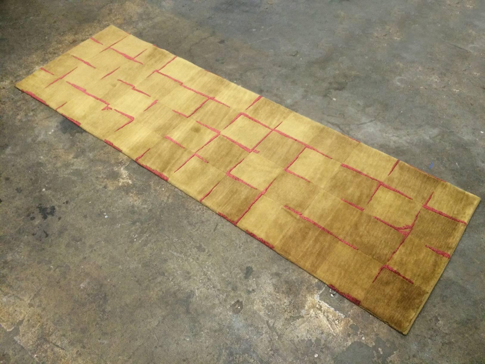This handmade Pakistani runner is made using two different types of wool. The pattern is based on an image of tiles or stone blocks with the red wool taking on the role of grout.