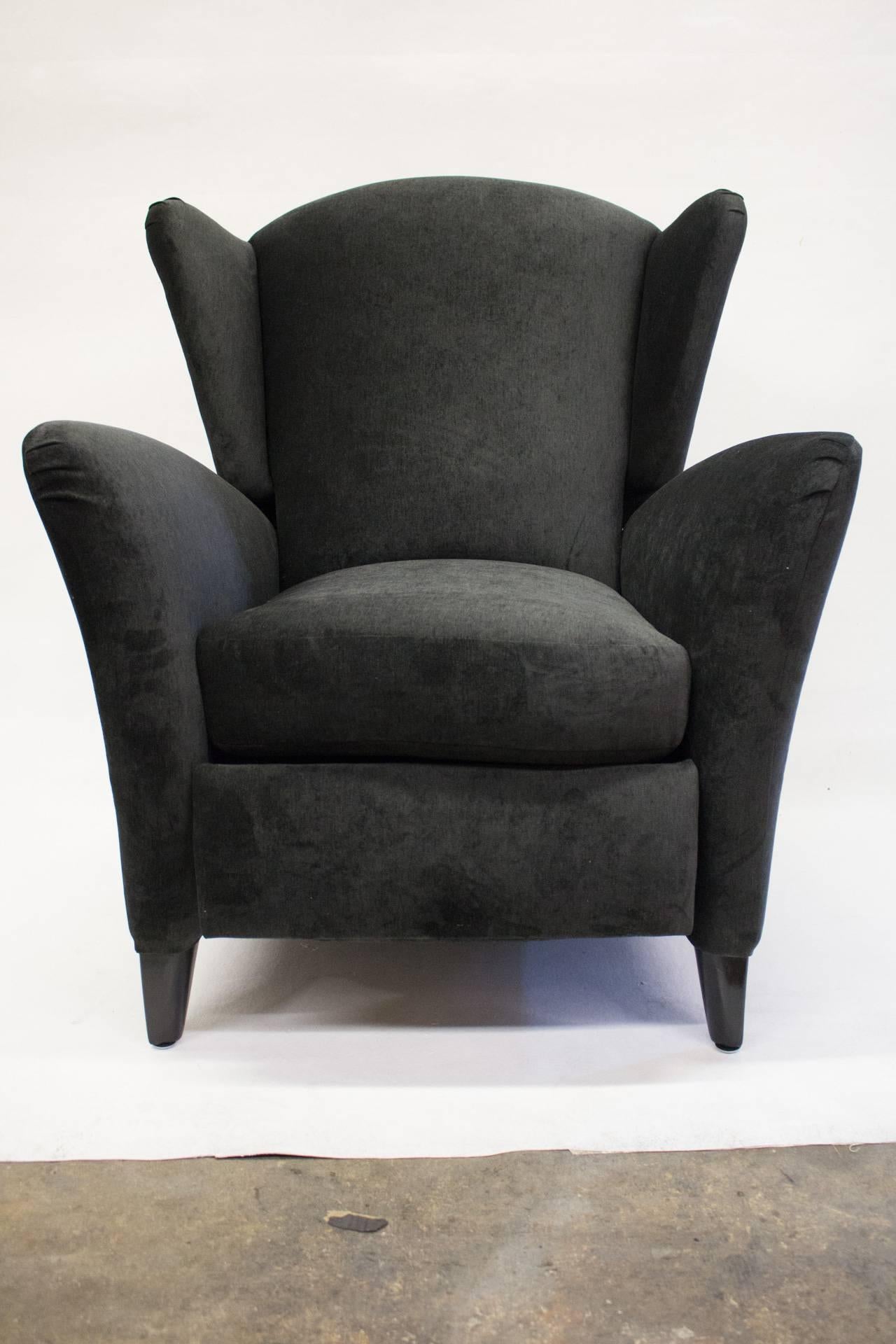 This Mid-Century reclining chair is upholstered in a thin black velvet with a high back with wings. It features black stained tapered wood feet. The back flares out to accentuate the comfort.