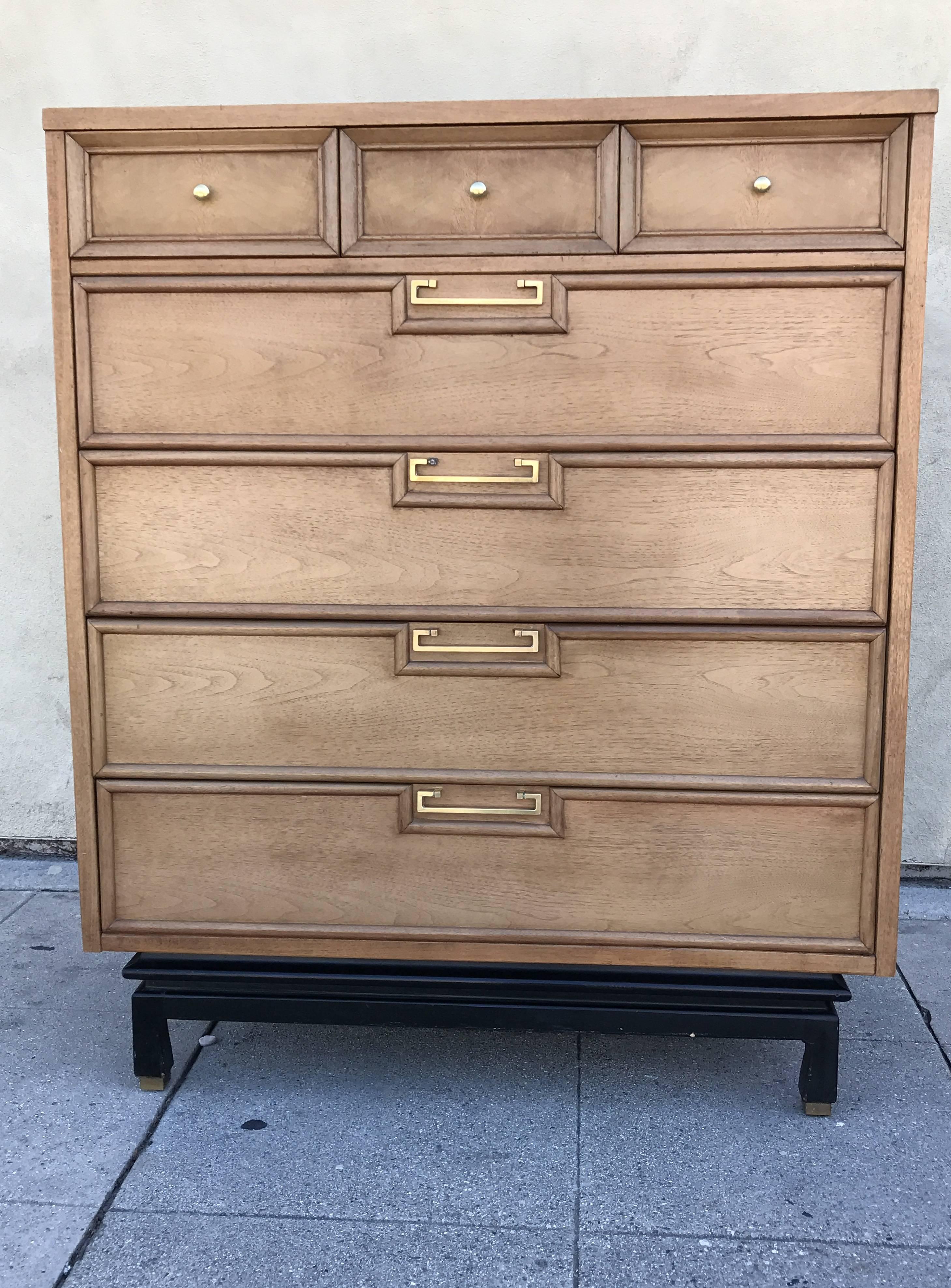 1960s walnut tall boy from Americans of Martinsville. Top section divided into three separate drawers with four larger drawers below. Brass knobs and handles. The base is black stained walnut.